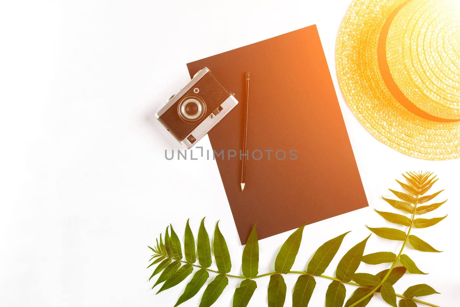 Straw hat with green leaves and old camera on white background, Summer background. Top view. Sun flare by nazarovsergey