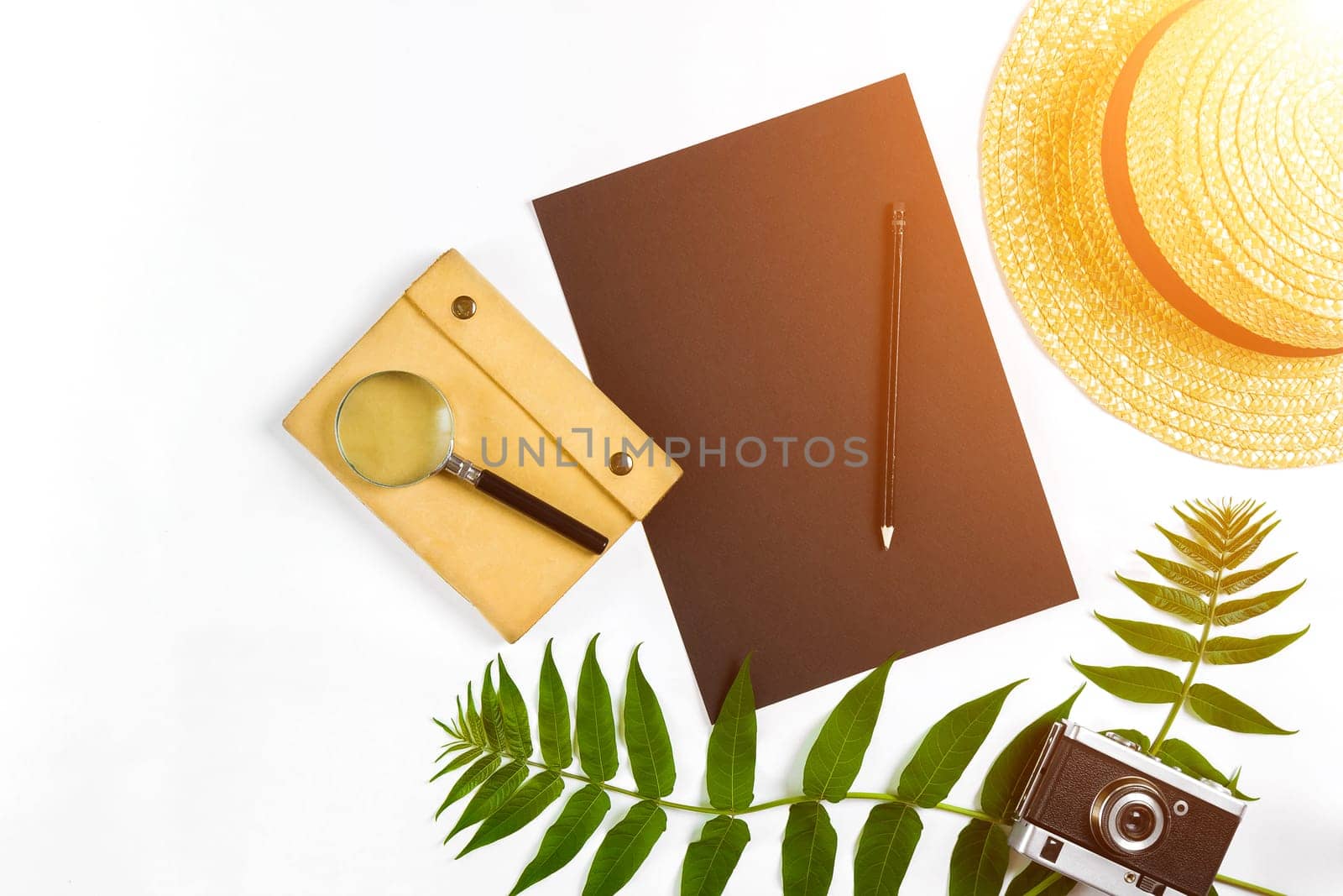 Straw hat with green leaves and old camera on white background, Summer background. Top view. Copy space. Still life. Flat lay. Sun flare