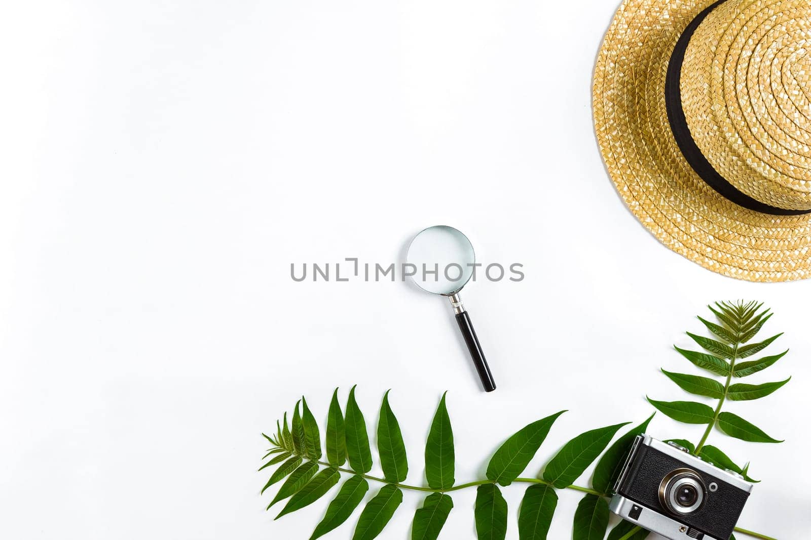 Straw hat with green leaves and old camera on white background, Summer background. Top view. Copy space. Still life. Flat lay