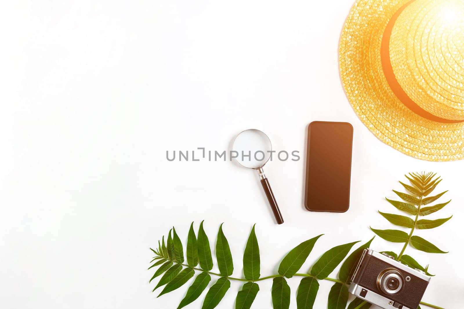 Straw hat with green leaves and old camera on white background, Summer background. Top view. Copy space. Still life. Flat lay. Sun flare