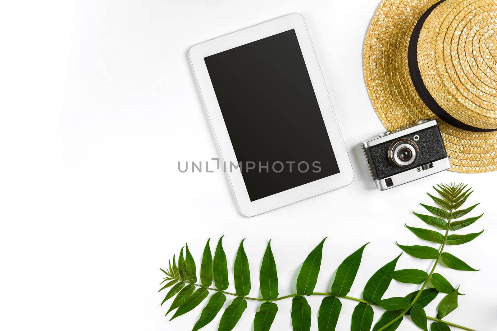 Straw hat with green leaves, tablet and old camera on white background, Summer background. Top view by nazarovsergey