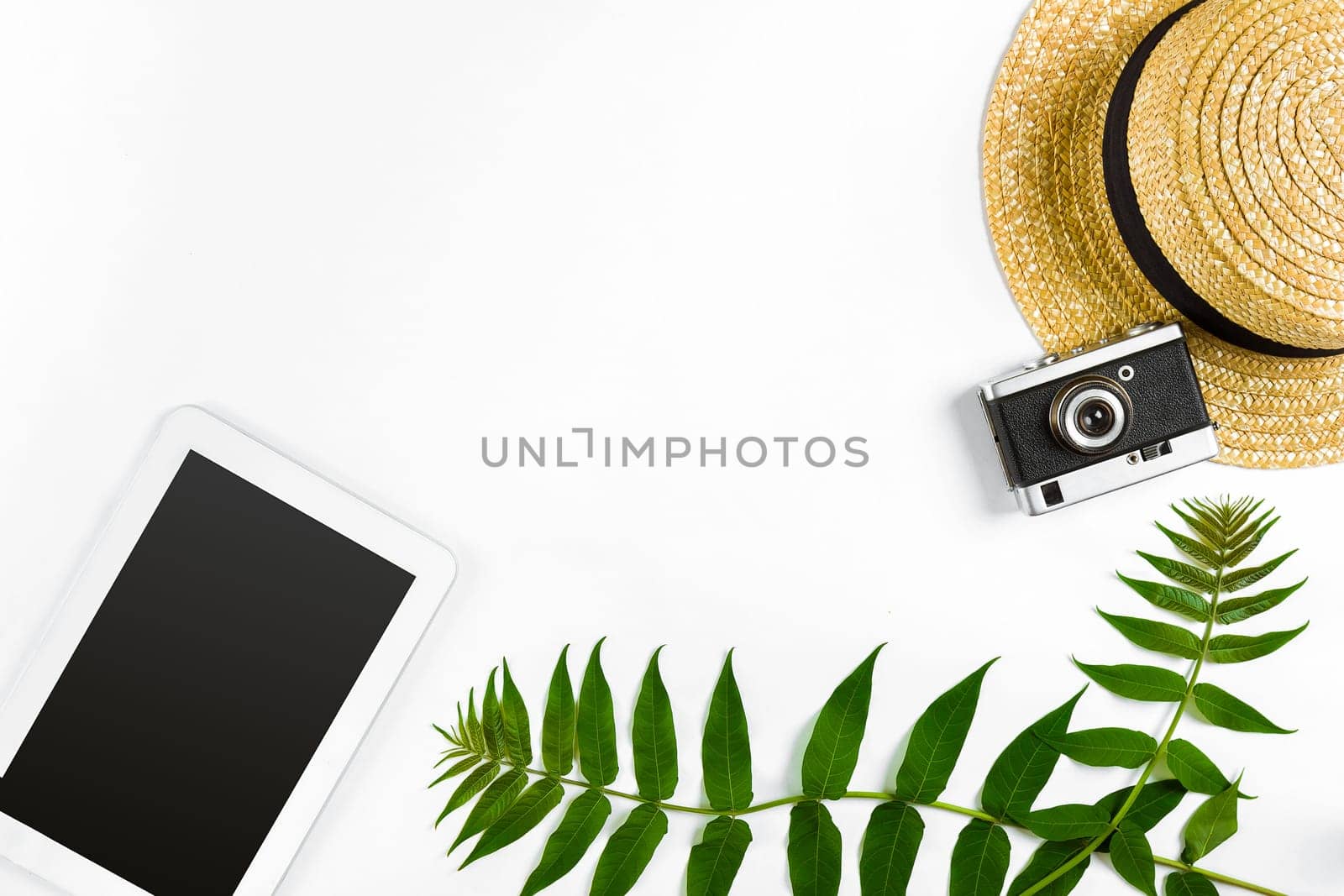 Straw hat with green leaves, tablet and old camera on white background, Summer background. Top view. Copy space. Still life. Flat lay