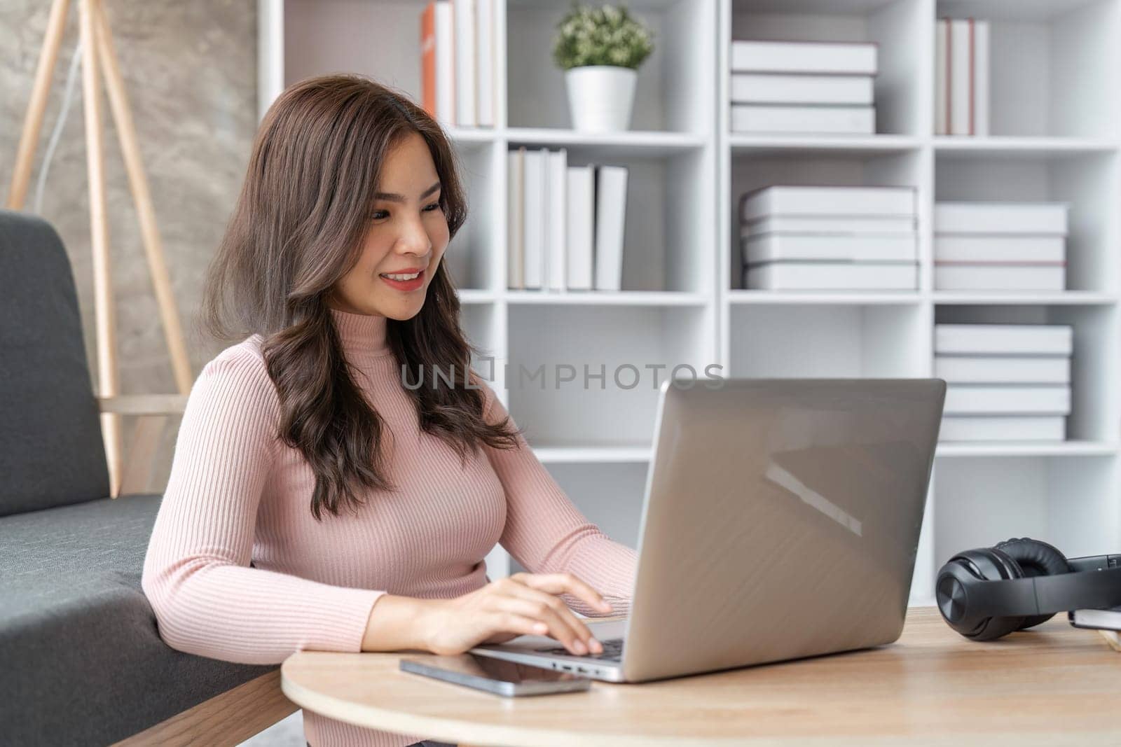 Young business freelance Asian woman working on laptop checking social media while sit on the sofa when relax in living room at home. Lifestyle at house concept.