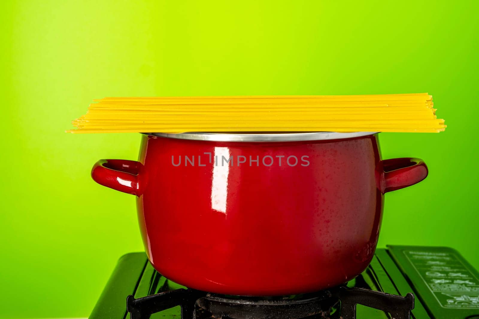 spaghetti in a saucepan. a beautiful red saucepan with spaghetti. cooking spaghetti in a saucepan on a gas stove. homemade Italian-style dinner. kitchen saucepan on a green background