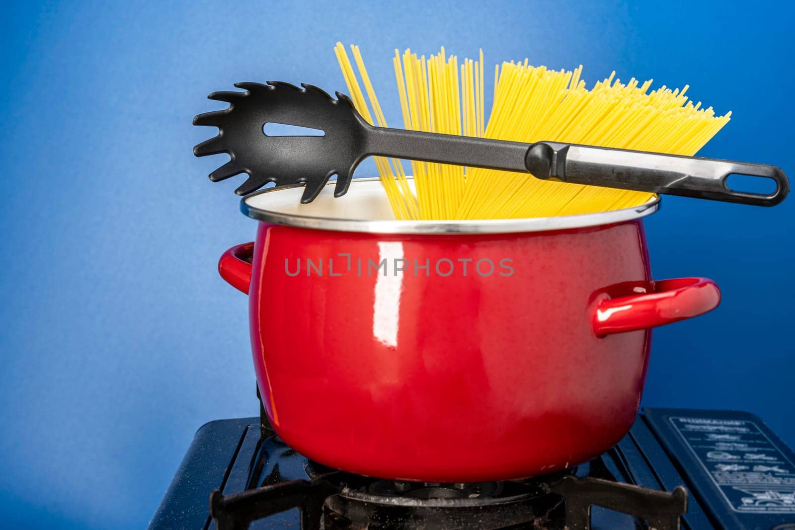 recipe. we cook ourselves. spaghetti in a saucepan. a beautiful red saucepan with spaghetti and skimmer. cooking spaghetti in a saucepan on a gas stove. homemade Italian-style dinner. kitchen saucepan on a blue background