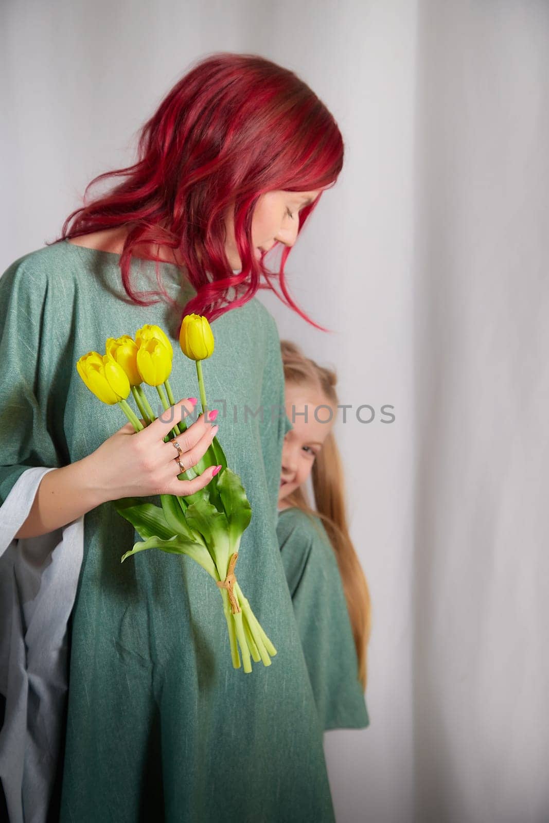 Beautiful woman with red hair in yellow dress on light background holds tulips. Inernational woman's day 8 March