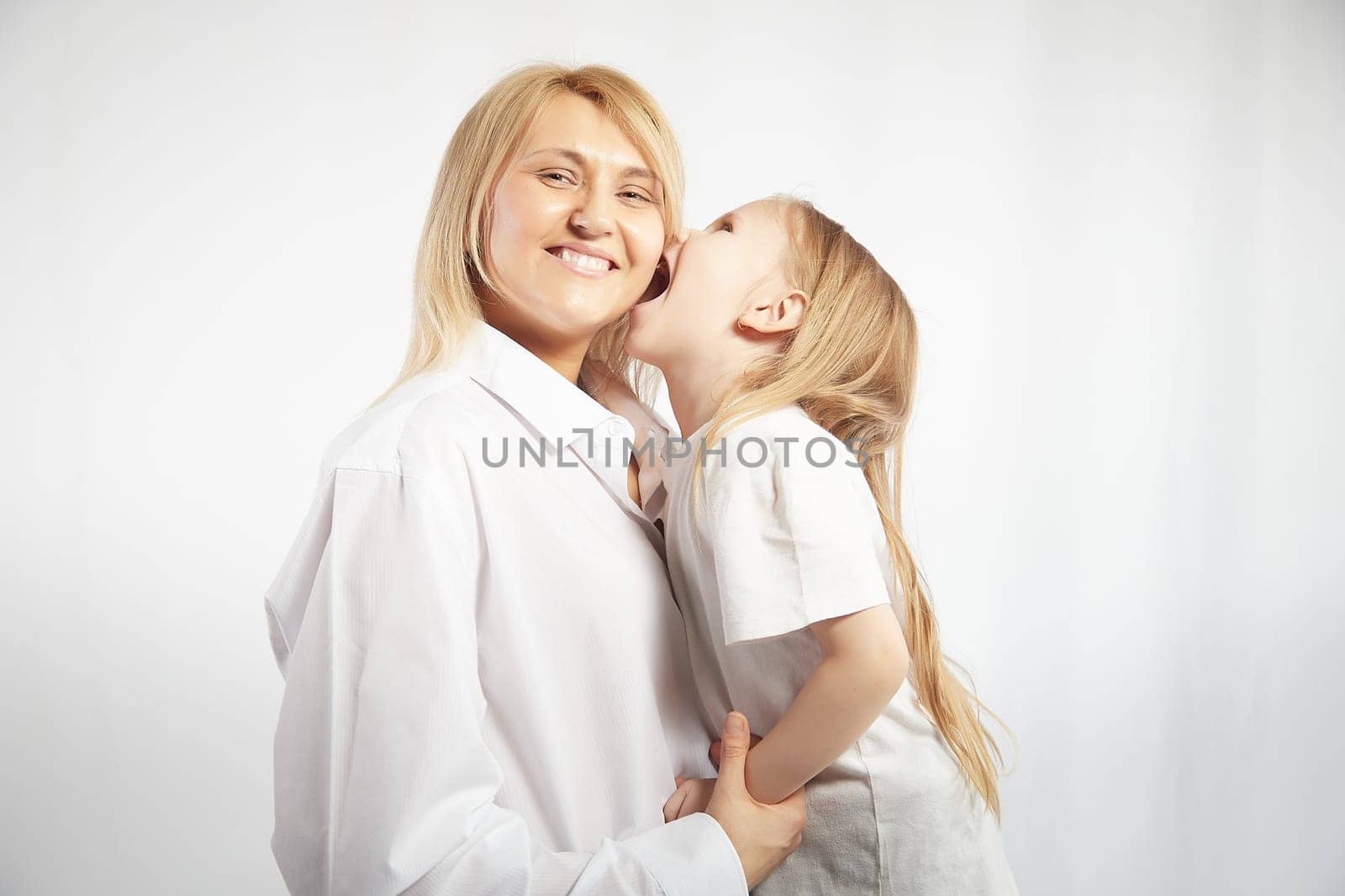 Portrait of blonde mother and daughter who having communicate and play on a white background. Mom and little girl models pose in the studio. The concept of love, friendship, caring in the family