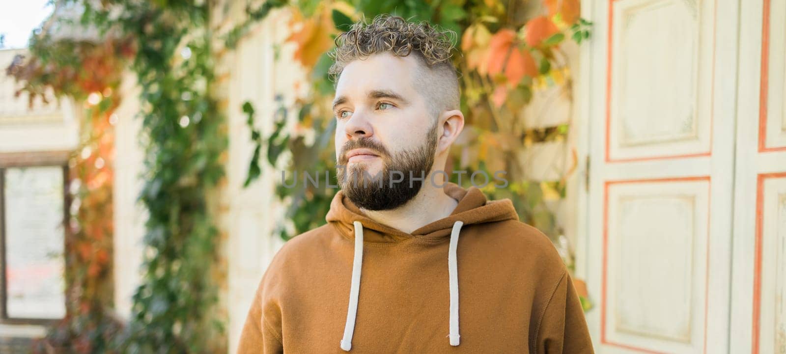 Banner Close up shot of curly European male with beard wears switshot outdoors copy space. Handsome man with crisp light hair. by Satura86