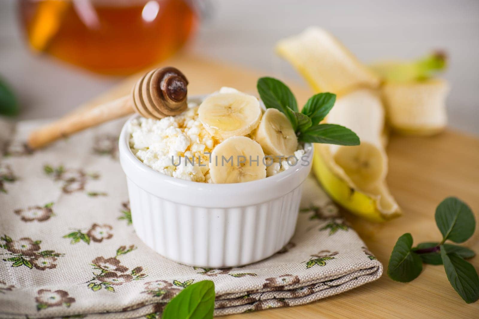 crumbly organic cottage cheese with honey and bananas in a ceramic bowl on the table
