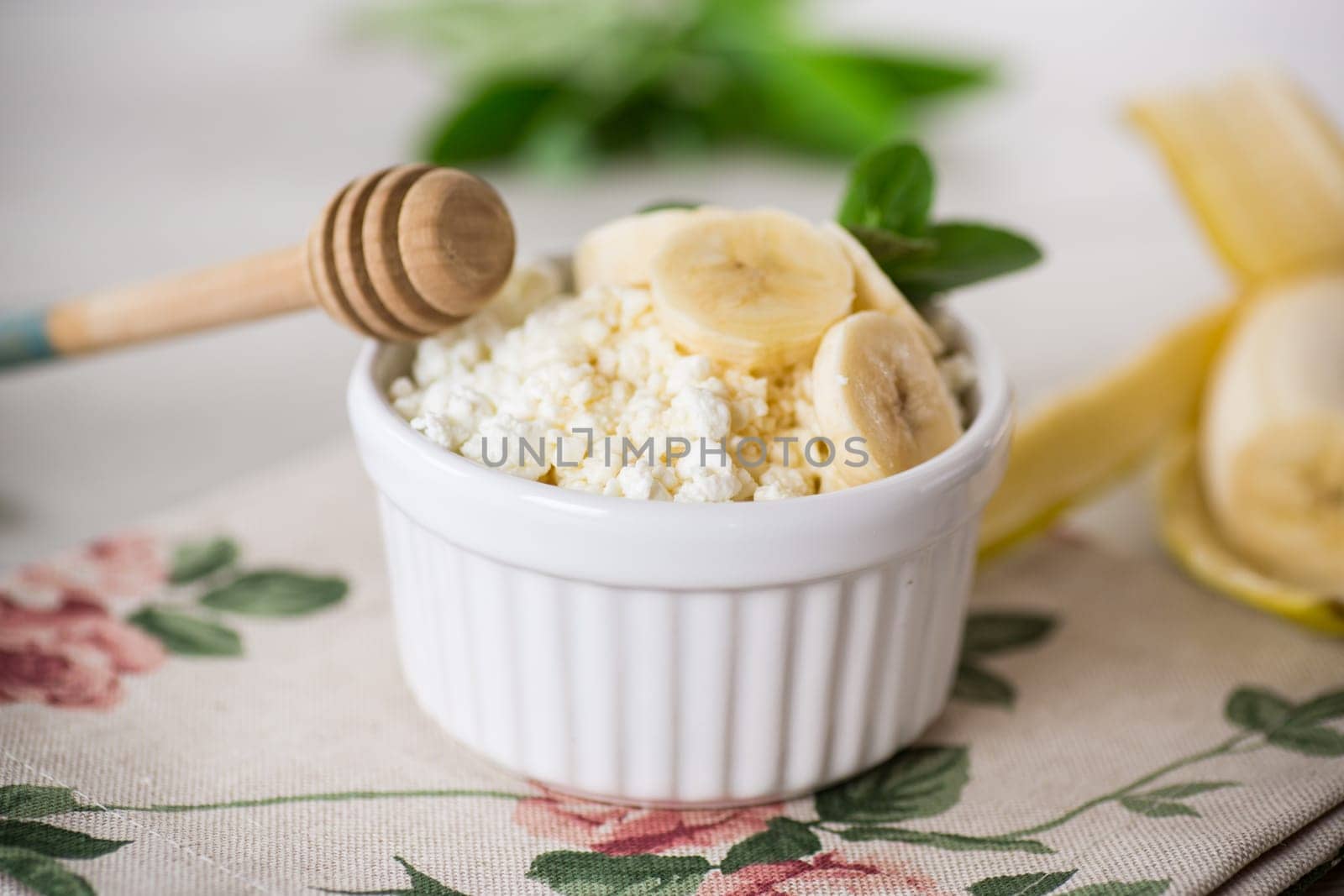 crumbly organic cottage cheese with honey and bananas in a ceramic bowl on the table