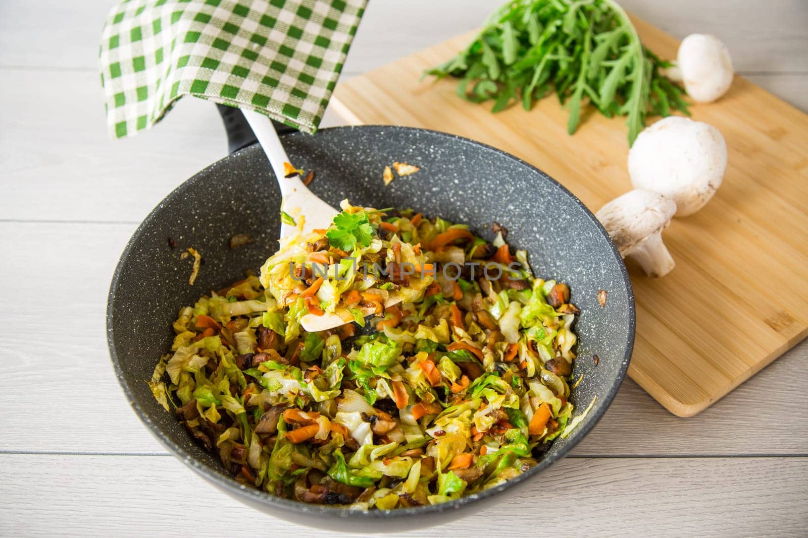 cabbage early fried with mushrooms, carrots and vegetables in a frying pan.