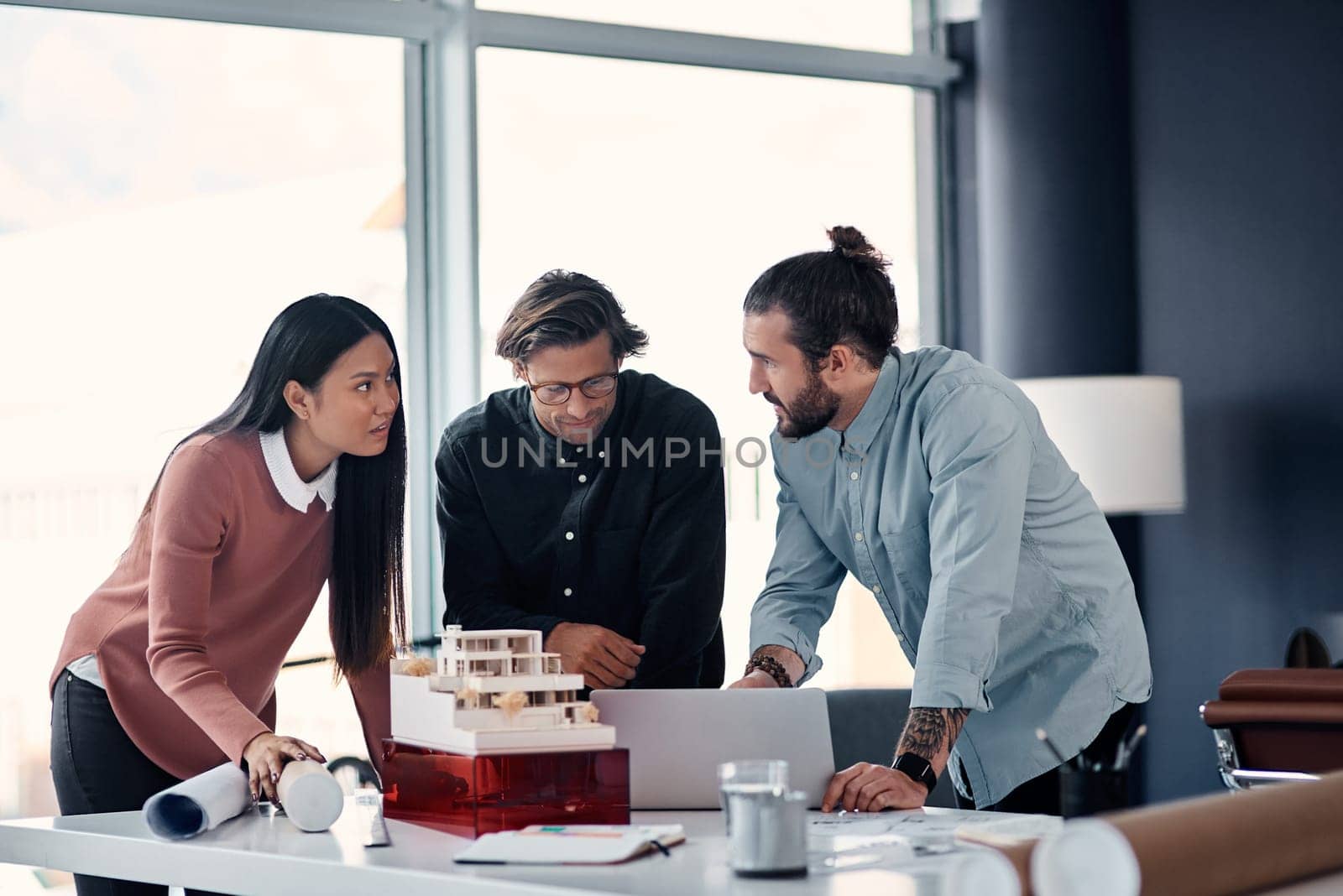 Effective communication is key when working together with colleagues. three young architects using a laptop while working together in their office. by YuriArcurs