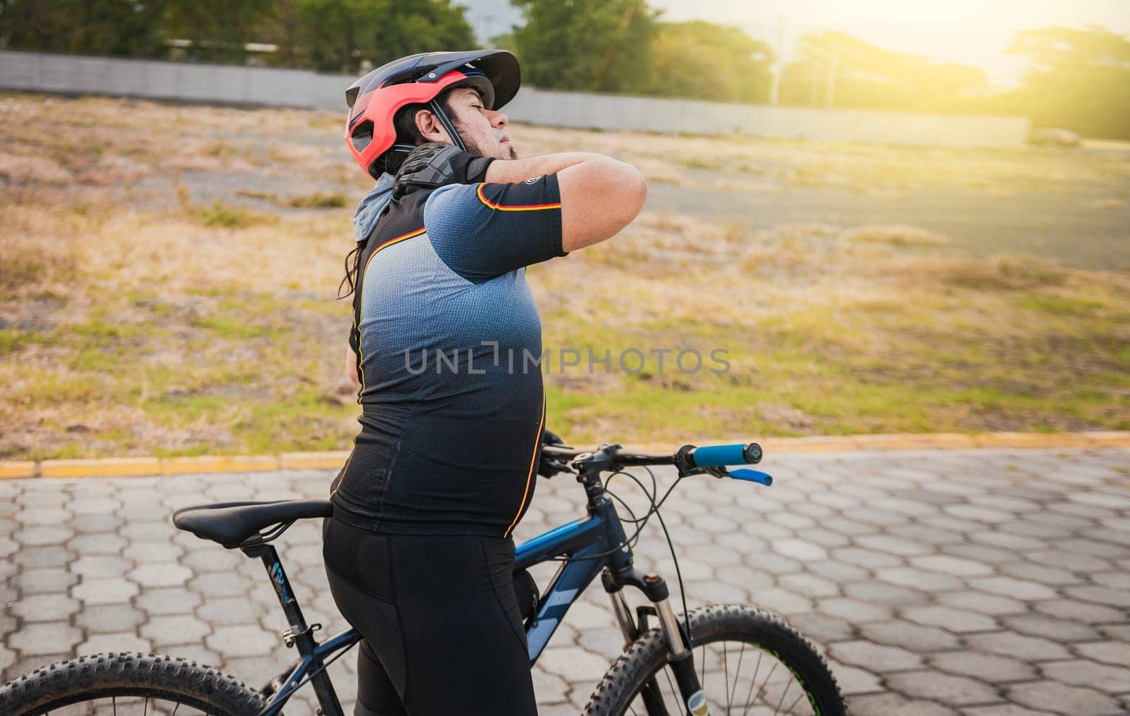 Sporty cyclist having neck pain while riding a bike. Male cyclist with neck pain outdoors