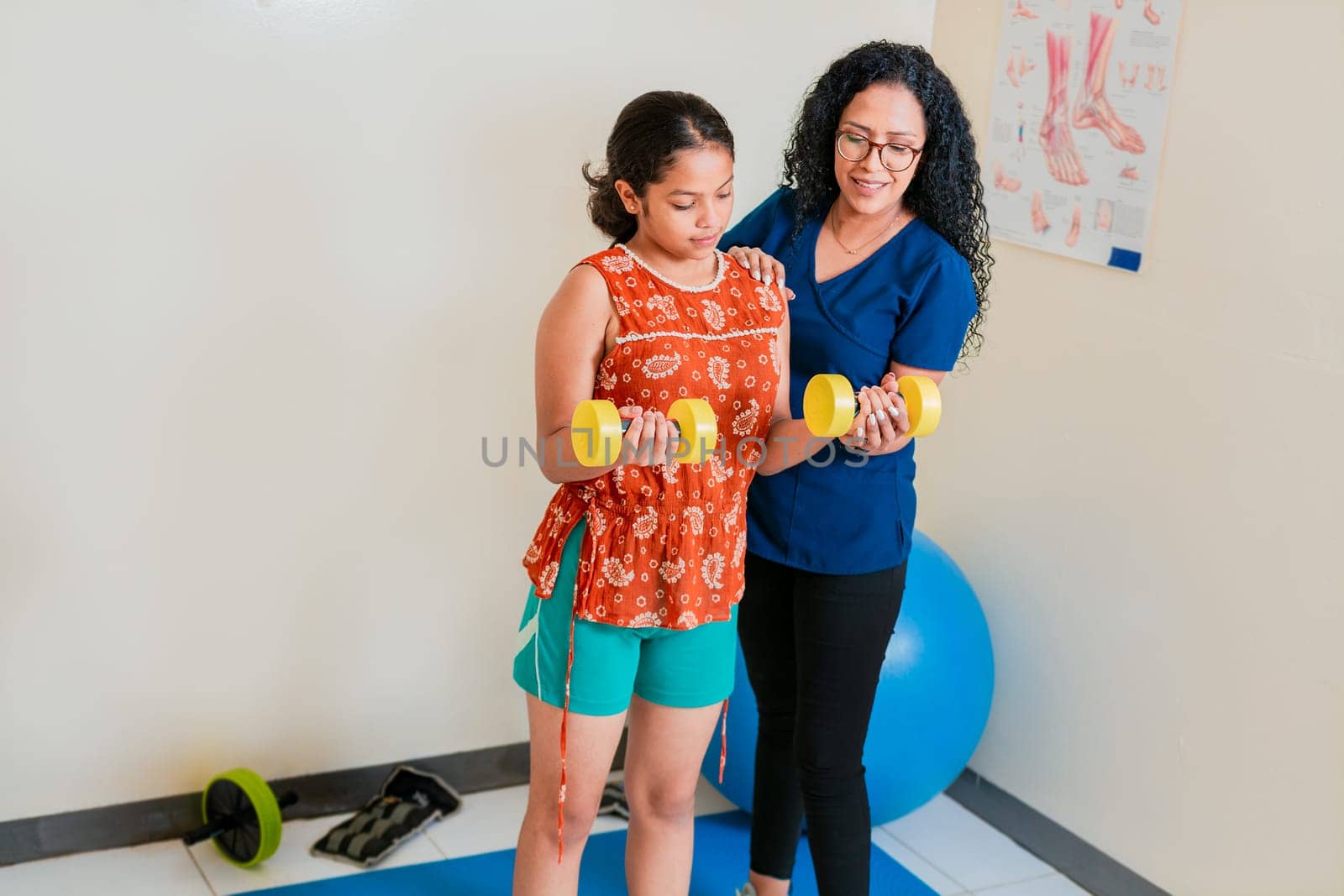 Physiotherapist assisting female patient with dumbbells on rehab ball. Rehabilitation physiotherapy with dumbbells by isaiphoto