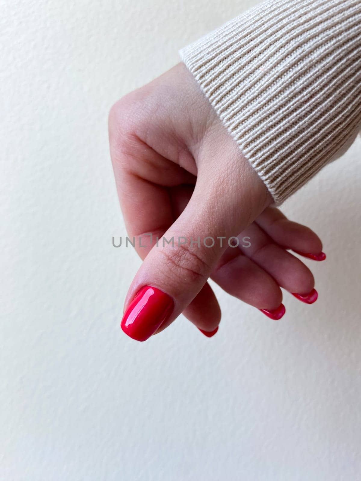 Red nail professional manicure, woman hand, beige sleeve. High quality photo