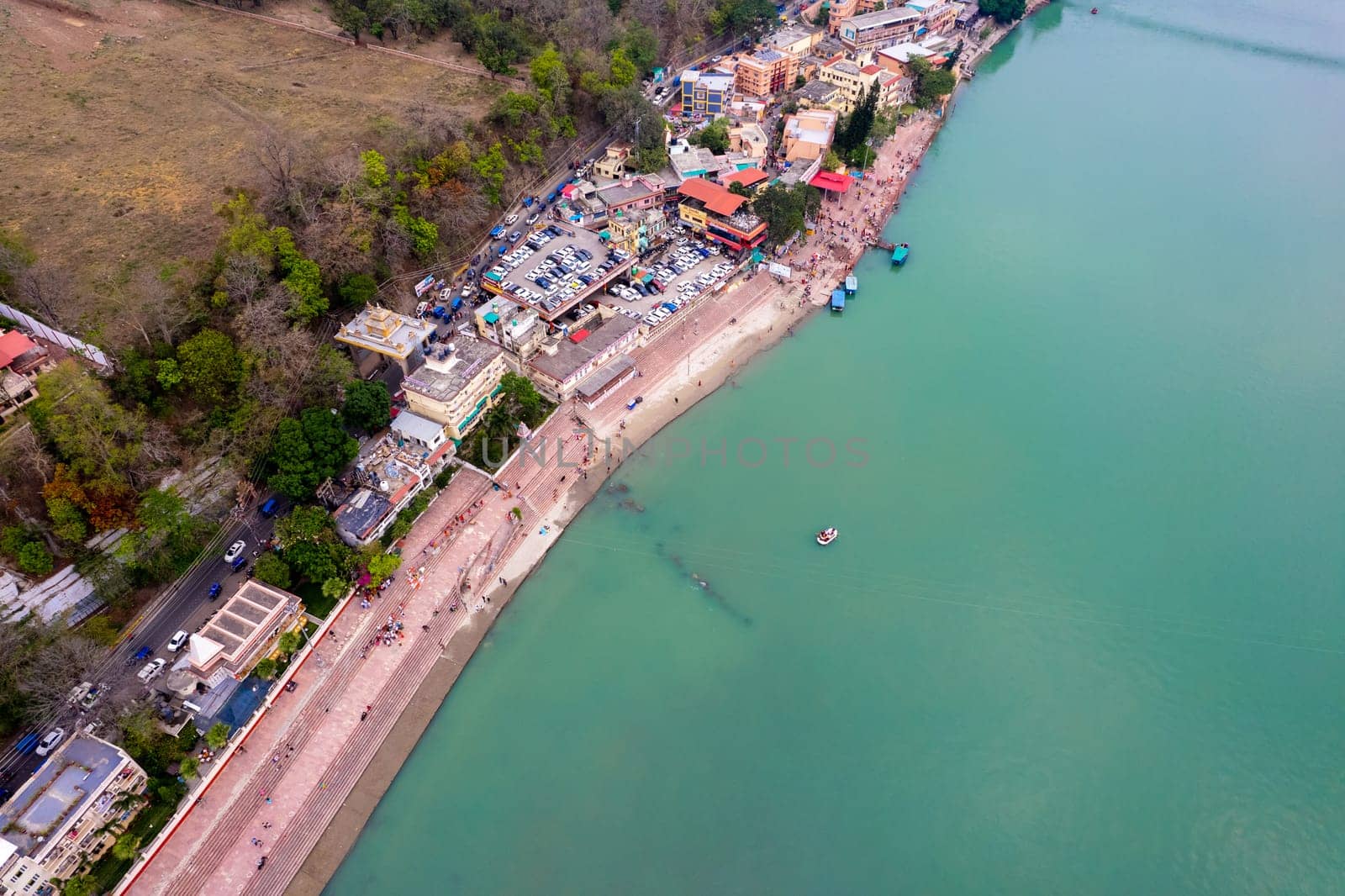 aerial drone shot of blue water of river ganga stretching into distance with steps stairs on the ghat bank of the river with temple and houses in India
