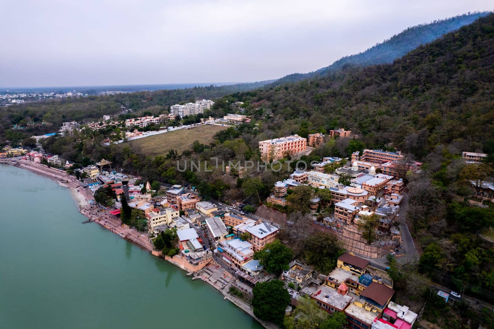 aerial drone shot of buildings apartments and temples on bank of ganga in the middle of dense trees on himalaya mountains in rishikesh haridwar in uttarakhand India