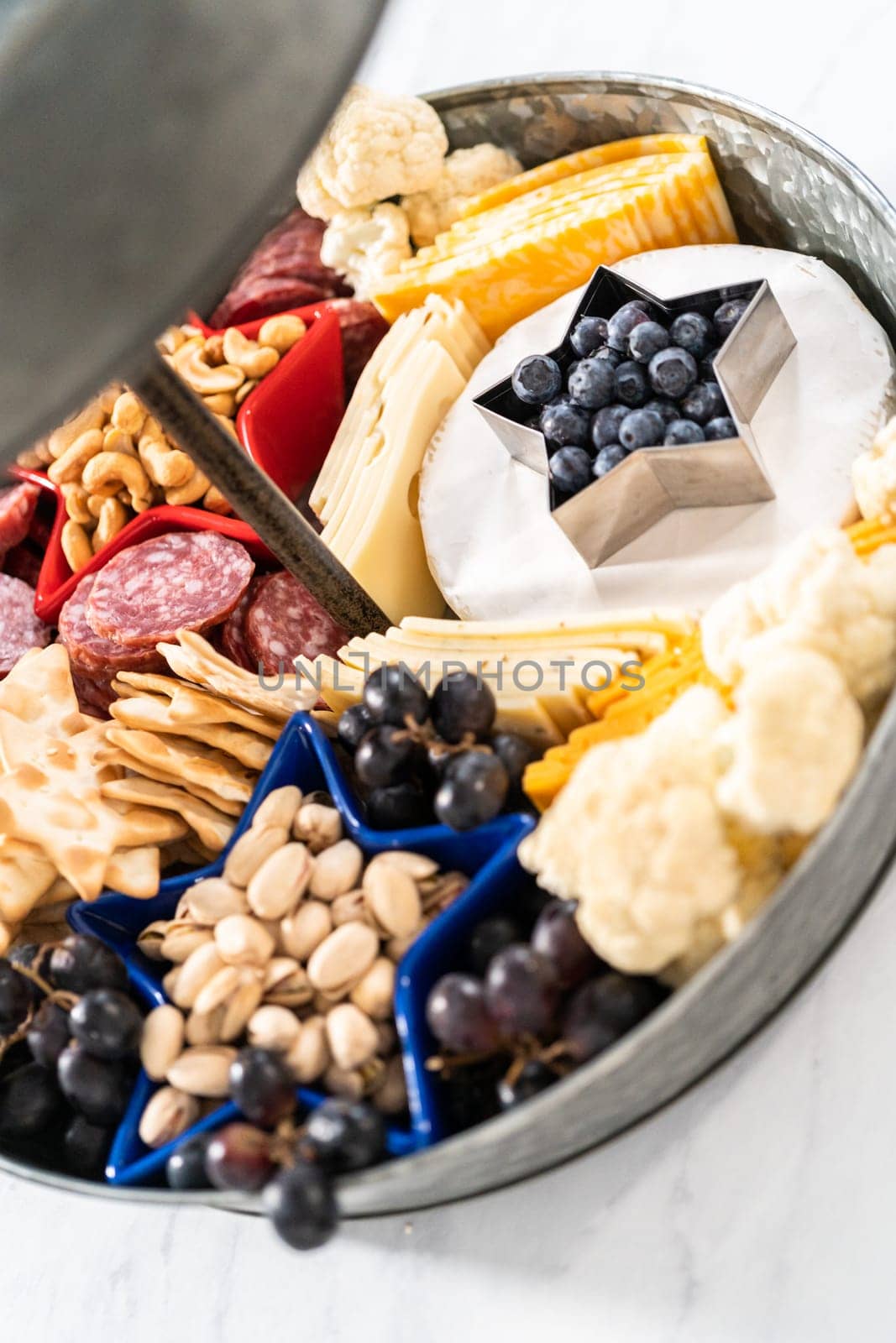 July 4th charcuterie board on a two-tiered serving metal stand filled with cheese, crackers, salami, and fresh fruits