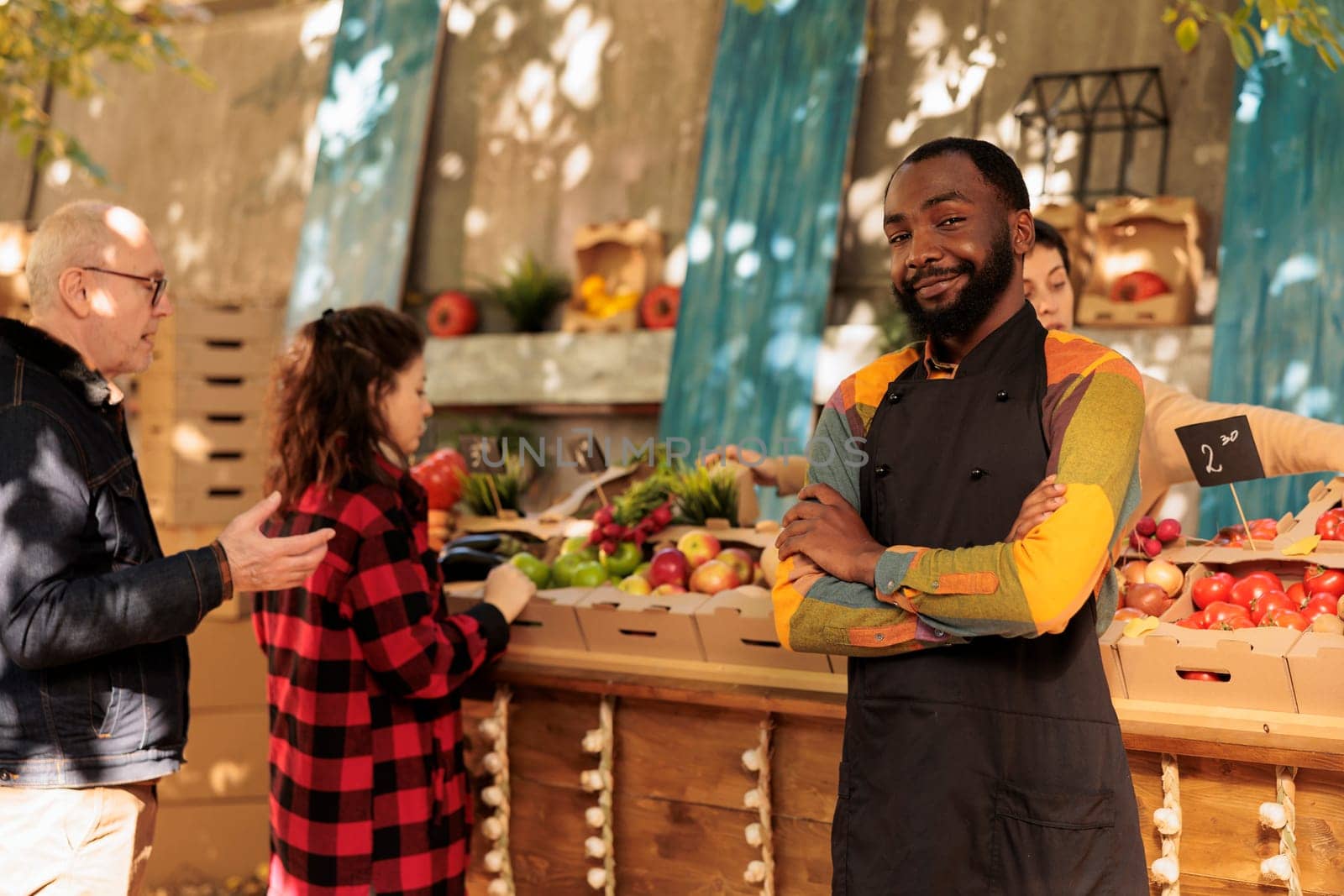 African american farmer standing next to food marketplace stand, selling healthy organic products. Young man with fresh natural fruits and vegetables, seasonal locally grown veggies.