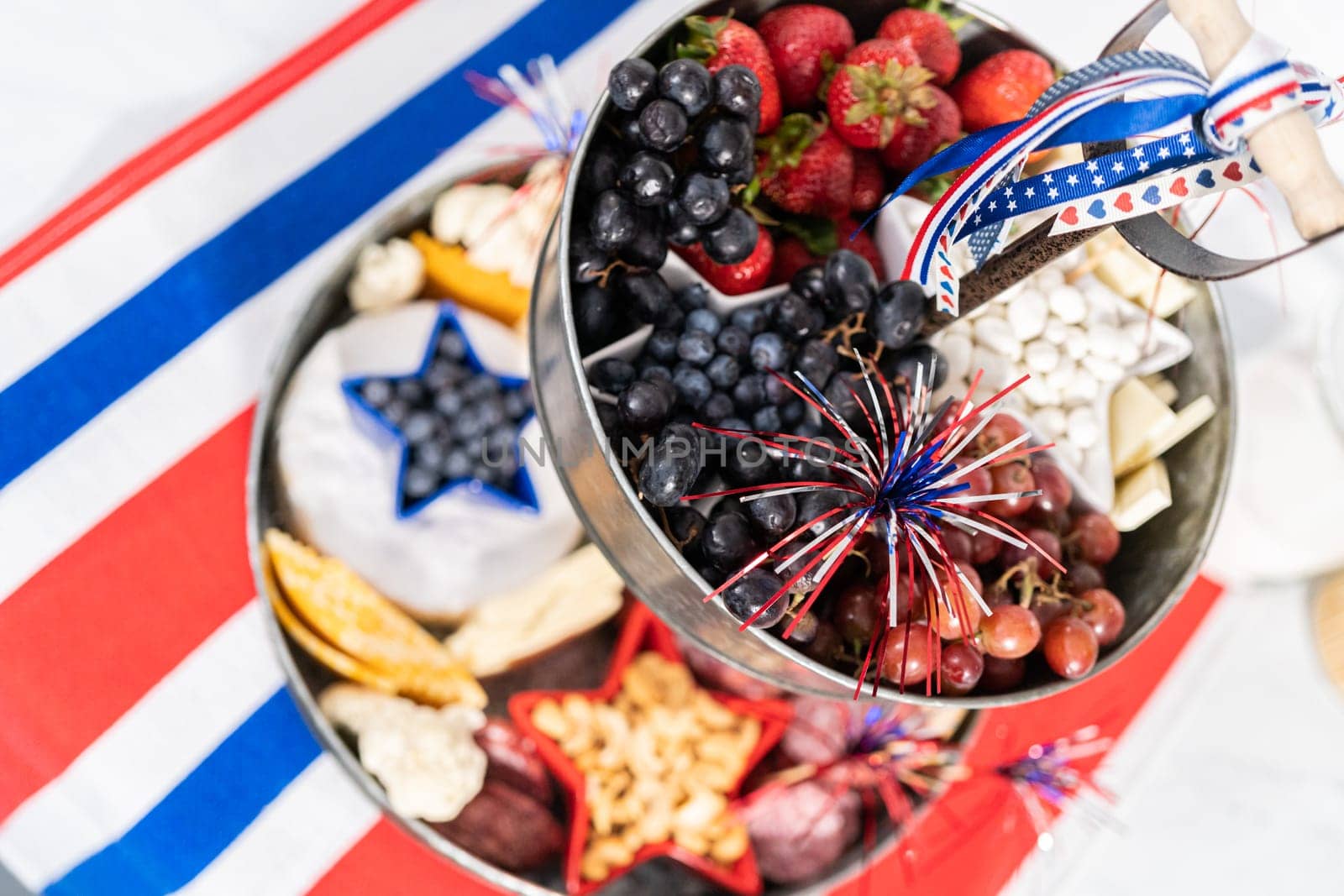 July 4th charcuterie board on a two-tiered serving metal stand filled with cheese, crackers, salami, and fresh fruits