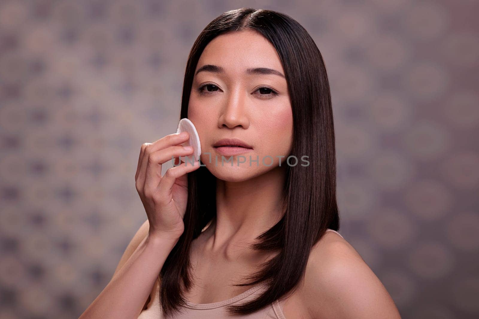 Woman using cotton pad to remove facial foundation cream by DCStudio