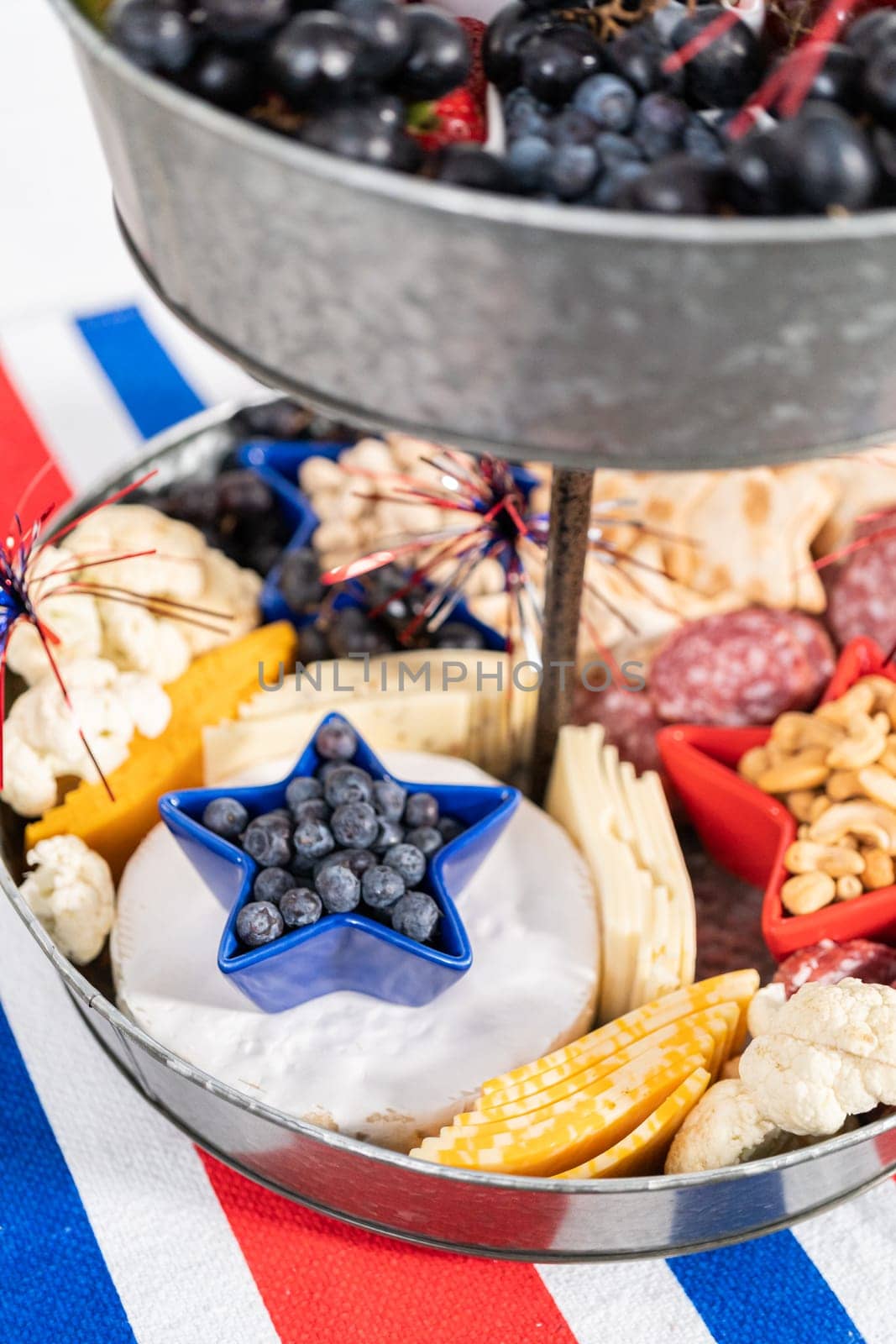 July 4th charcuterie board on a two-tiered serving metal stand filled with cheese, crackers, salami, and fresh fruits