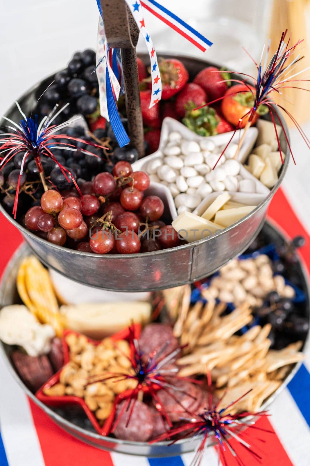 July 4th charcuterie board on a two-tiered serving metal stand filled with cheese, crackers, salami, and fresh fruits