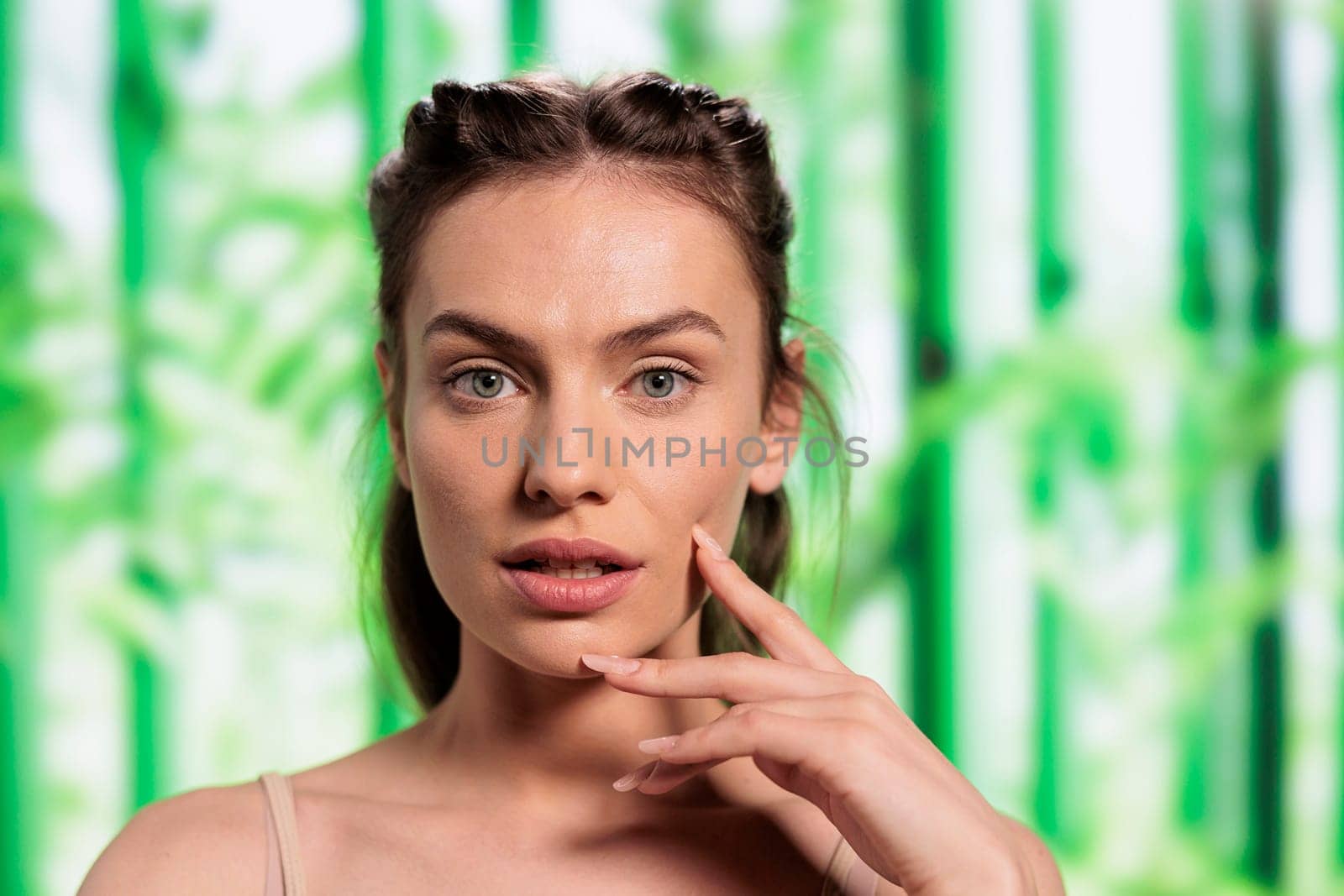 Young caucasian skincare model posing with fingers on face portrait. Natural beautiful woman showing glowing skin after organic cosmetology treatment on bamboo background