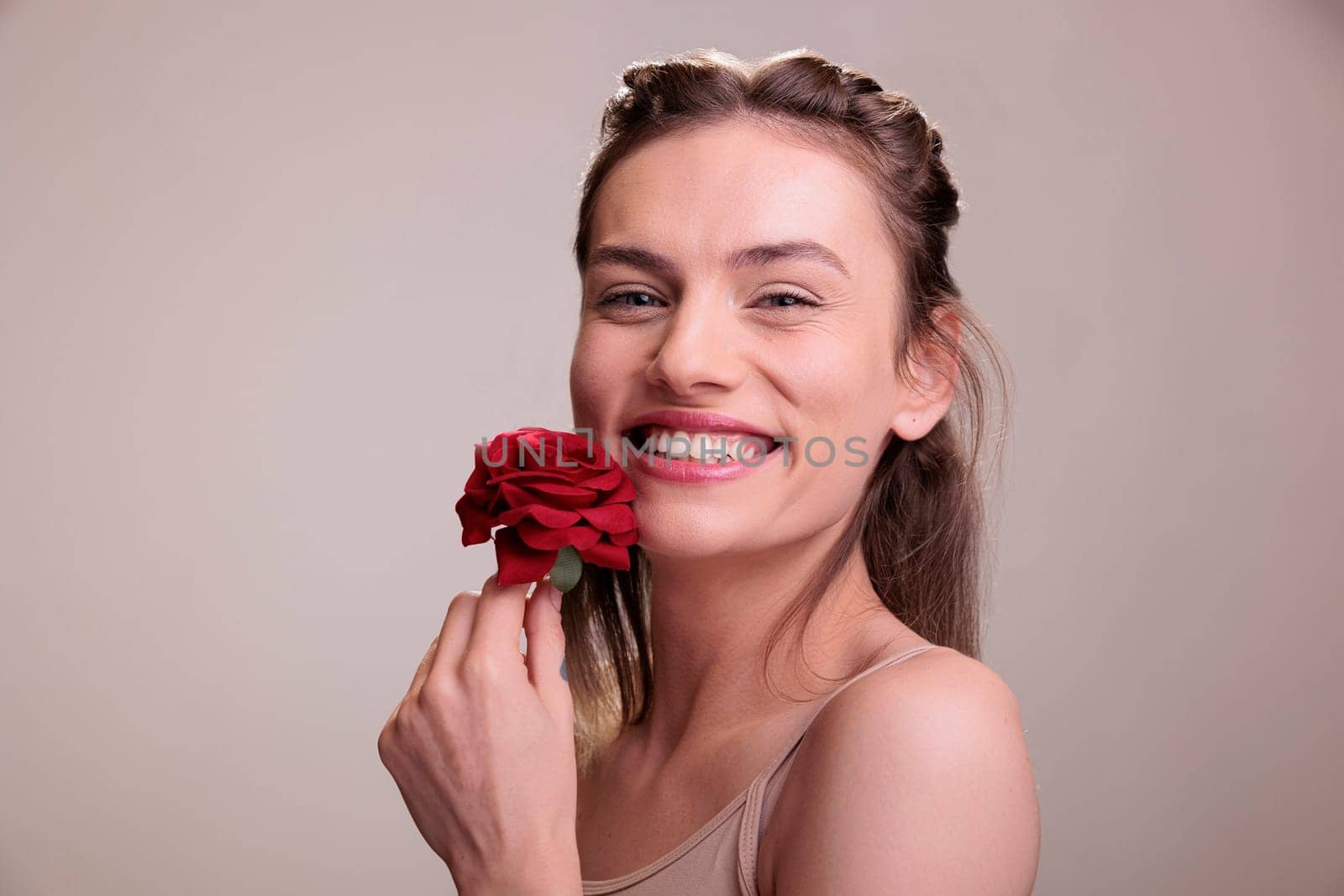 Laughing young woman posing with red rose gift portrait. Attractive cheerful caucasian blonde lady wearing nude makeup holding flower romantic present and expressing positive emotion