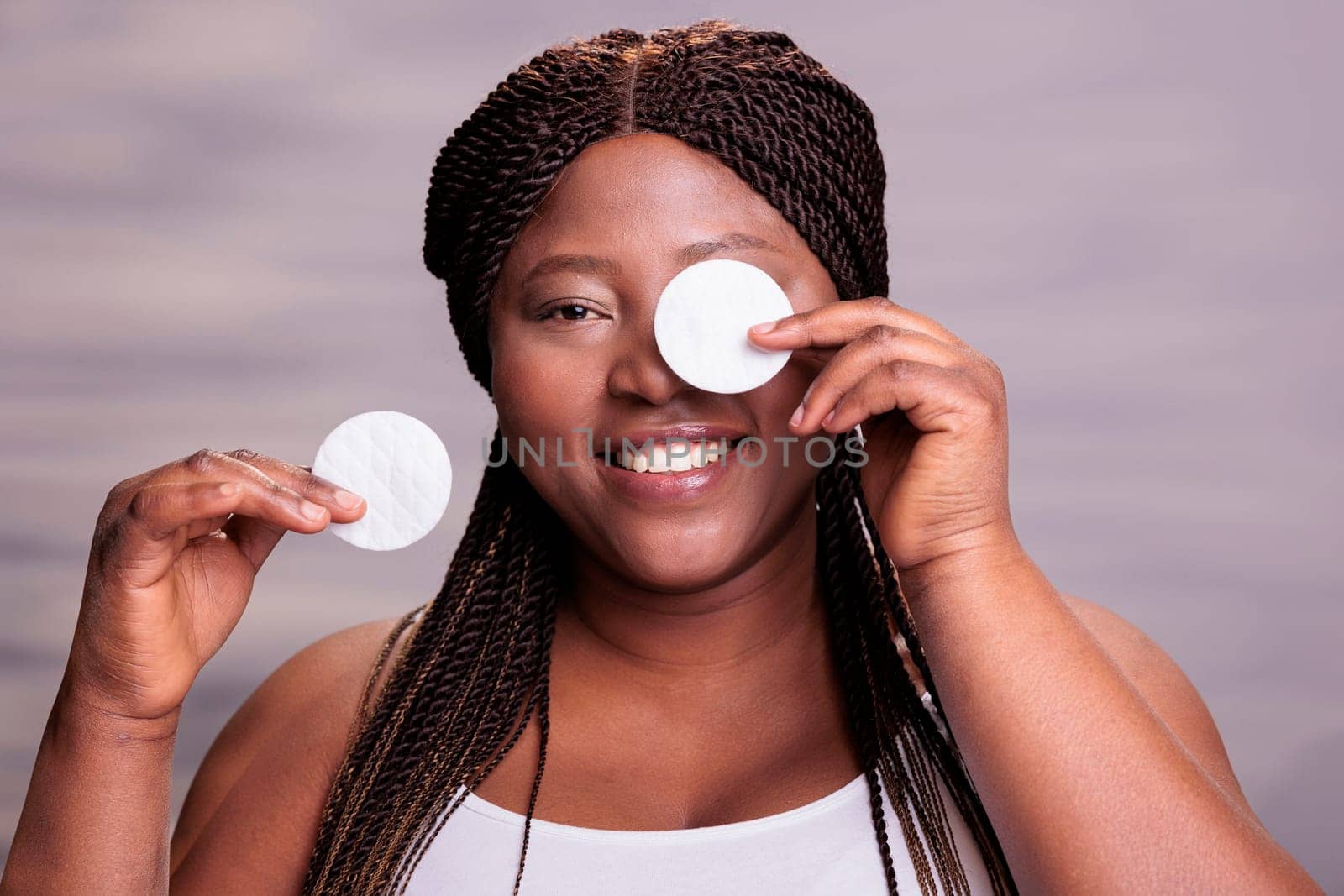 African american woman removing eyes make up with cotton disk pads, doing skincare routine for healthy skin. Smiling plus size model cleaning face from decorative cosmetics portrait