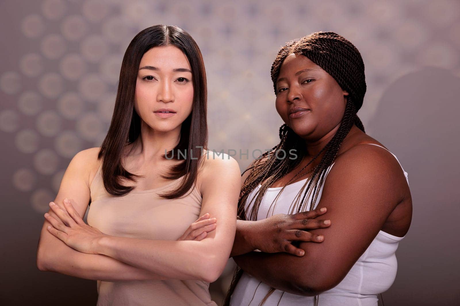 Confident diverse women posing with crossed hands, showing success gesture and looking at camera. African american and asian models with different body types standing with folded arms