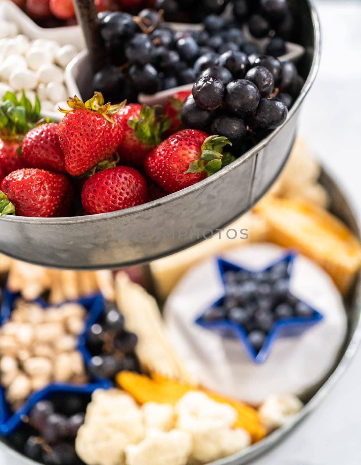 July 4th charcuterie board on a two-tiered serving metal stand filled with cheese, crackers, salami, and fresh fruits