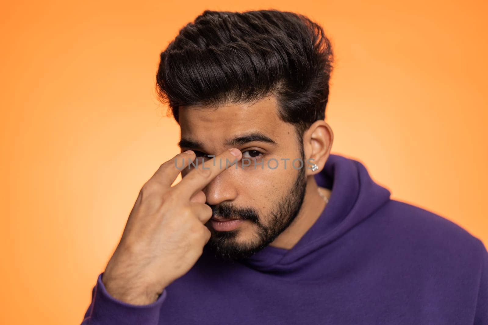 I am watching you. Young confident indian man pointing at his eyes and camera, show I am watching you gesture, spying on someone. Handsome bearded hindu guy isolated alone on orange studio background