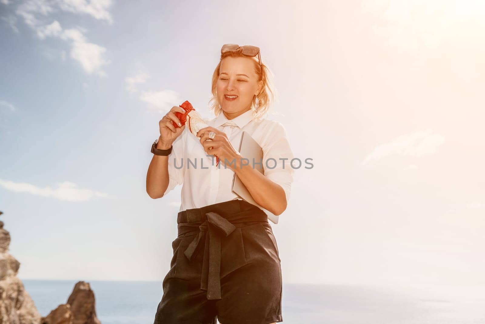 Digital nomad, Business woman working on laptop by the sea. Pretty lady typing on computer by the sea at sunset, makes a business transaction online from a distance. Freelance, remote work on vacation by panophotograph