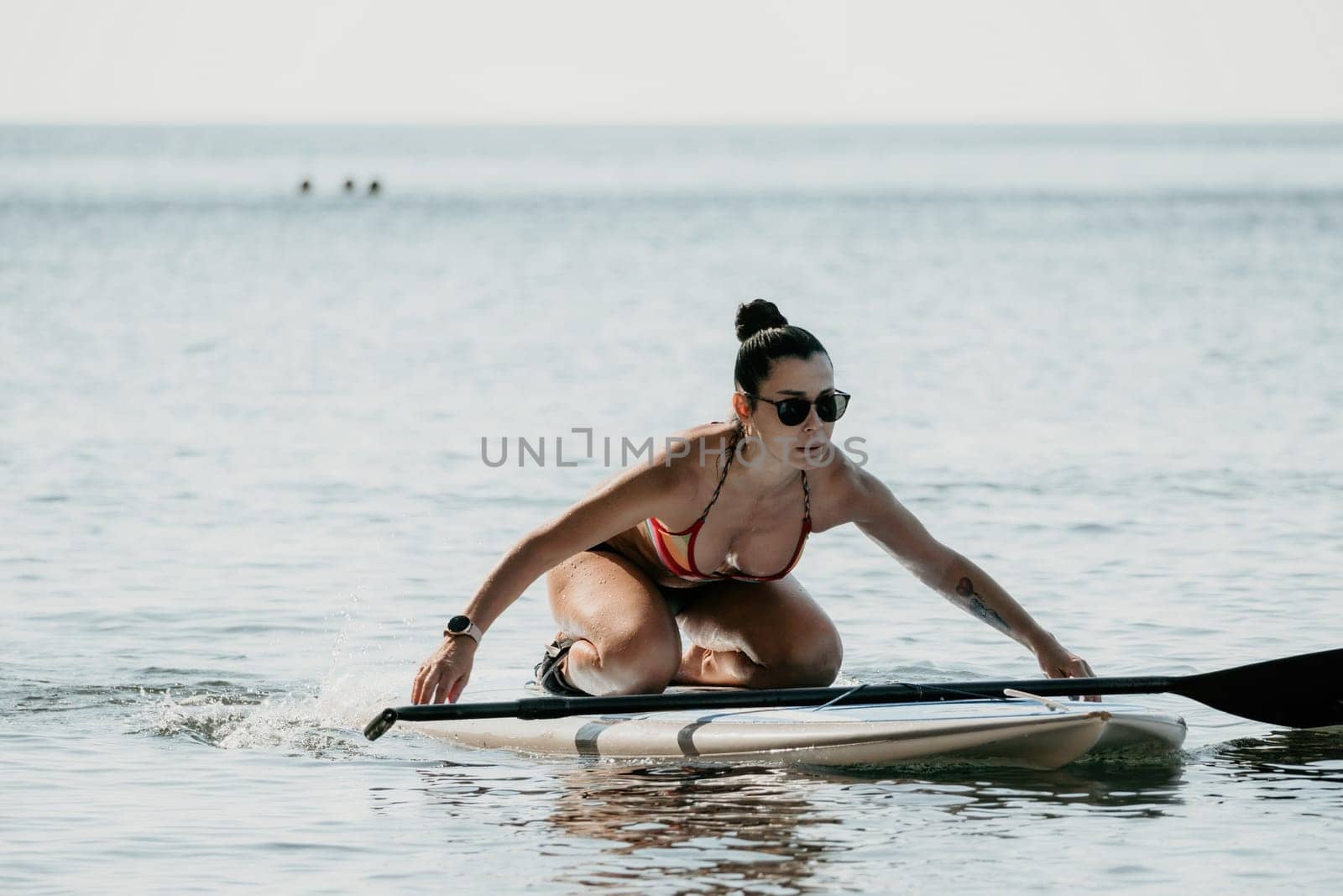 Sea woman sup. Silhouette of happy middle aged woman in rainbow bikini, surfing on SUP board, confident paddling through water surface. Idyllic sunset. Active lifestyle at sea or river