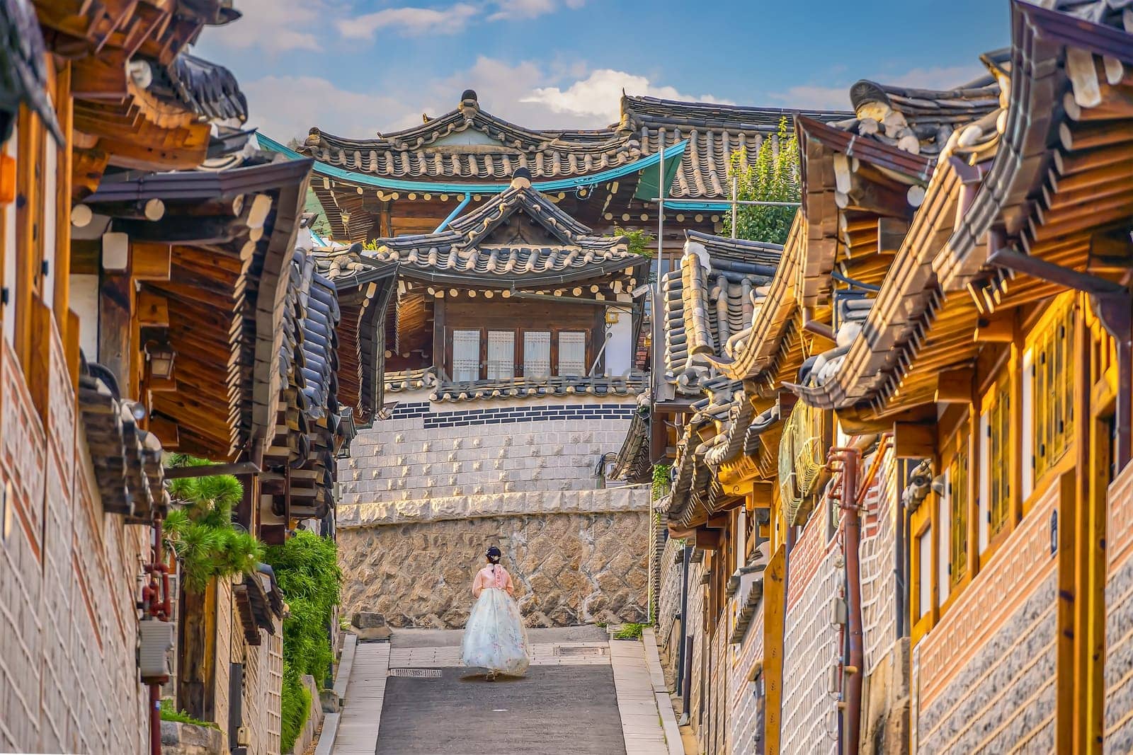 Girl wearing hanbok walking through Bukchon Hanok Village with Seoul city skyline, cityscape of South Korea at sunset