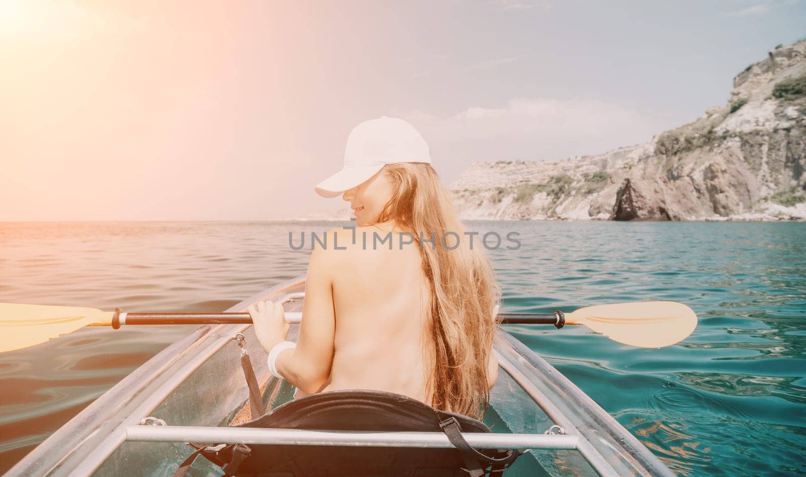 Woman in kayak back view. Happy young woman with long hair floating in transparent kayak on the crystal clear sea. Summer holiday vacation and cheerful female people having fun on the boat.