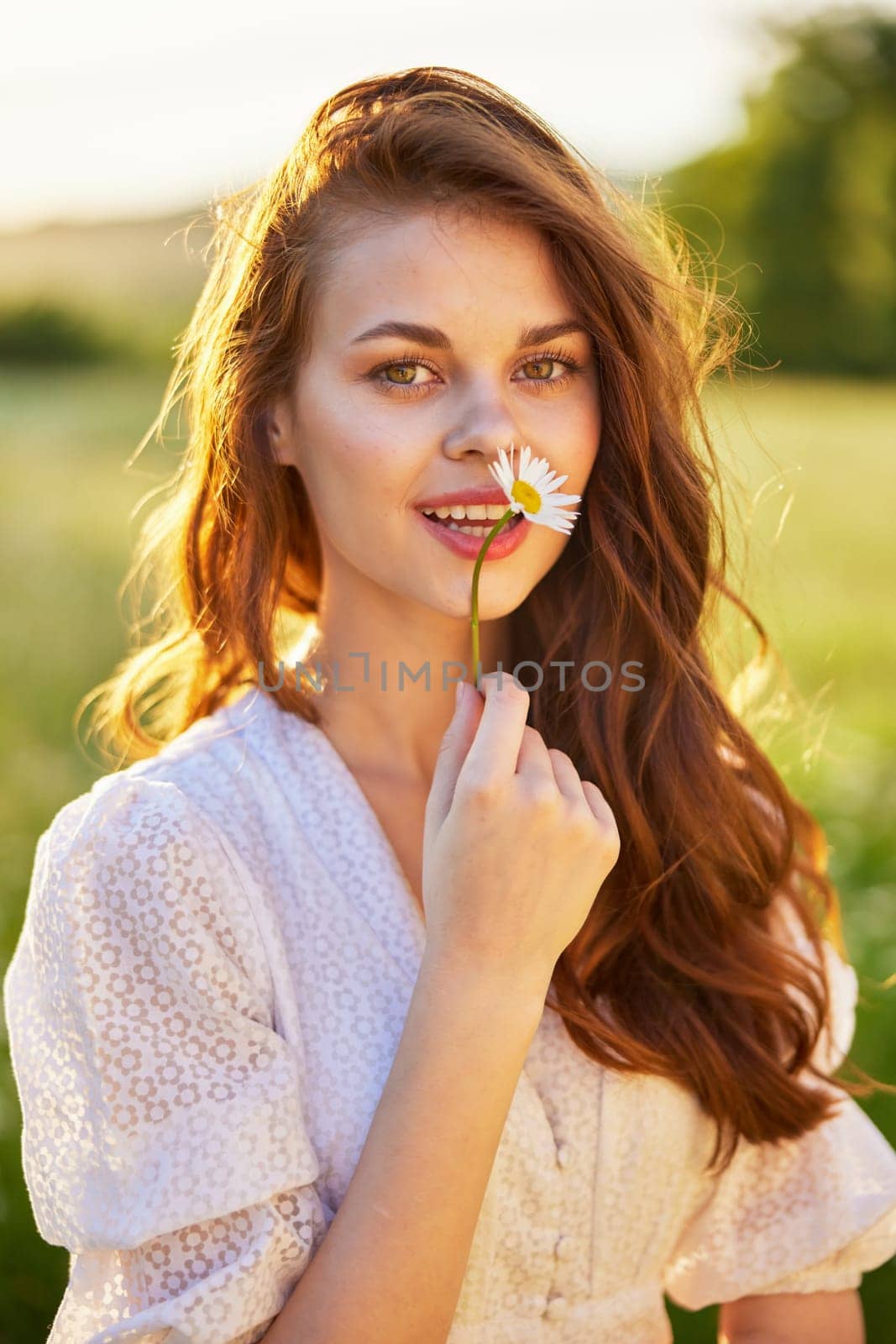 close portrait of a beautiful, laughing woman in a light dress holding a camomile near her face by Vichizh