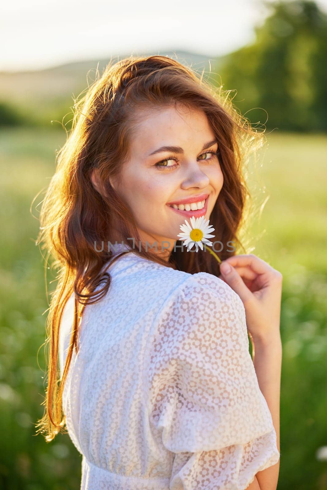 close portrait of a beautiful, laughing woman in a light dress holding a camomile near her face. High quality photo