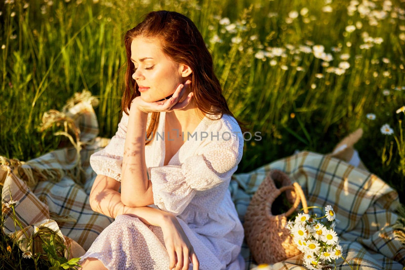 a beautiful woman in a light dress sits in the rays of the setting sun enjoying a warm day. High quality photo