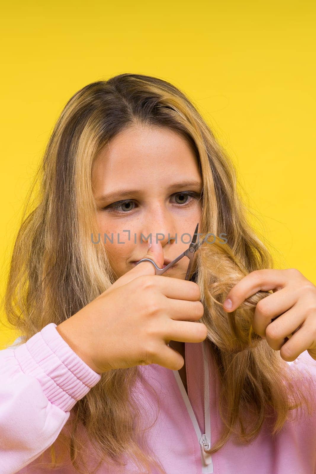 Child adorable girl hairdresser cutting long blonde hair with metallic scissors on a yellow