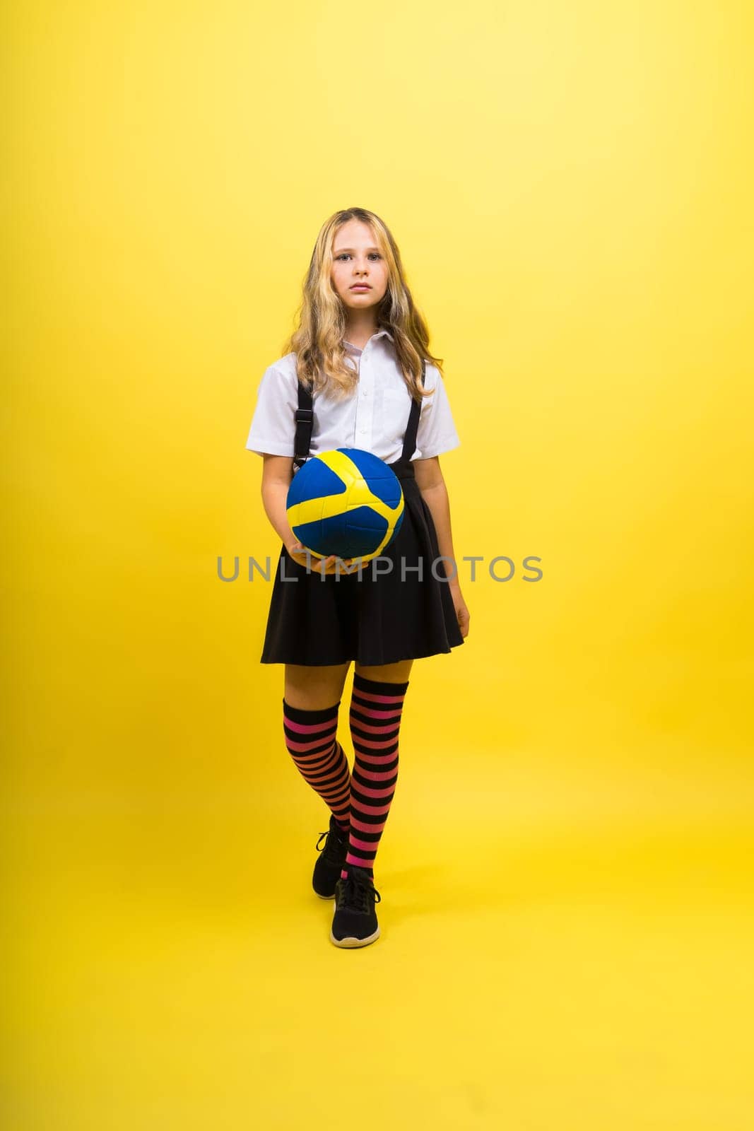 A teenager girl holds volleyball ball in hand and smiles on a red yellow background. Studio photo. by Zelenin