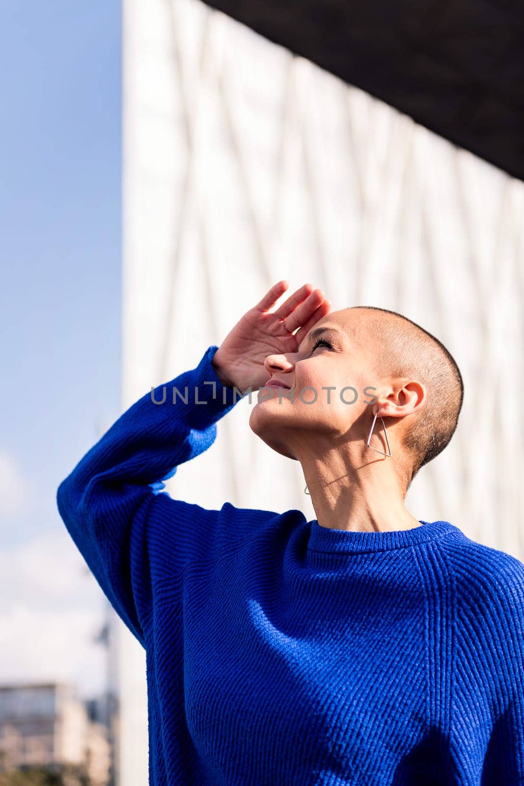 confident woman with shaved head smiling looking to the sky at city, concept of urban lifestyle and rebel style, copy space for text