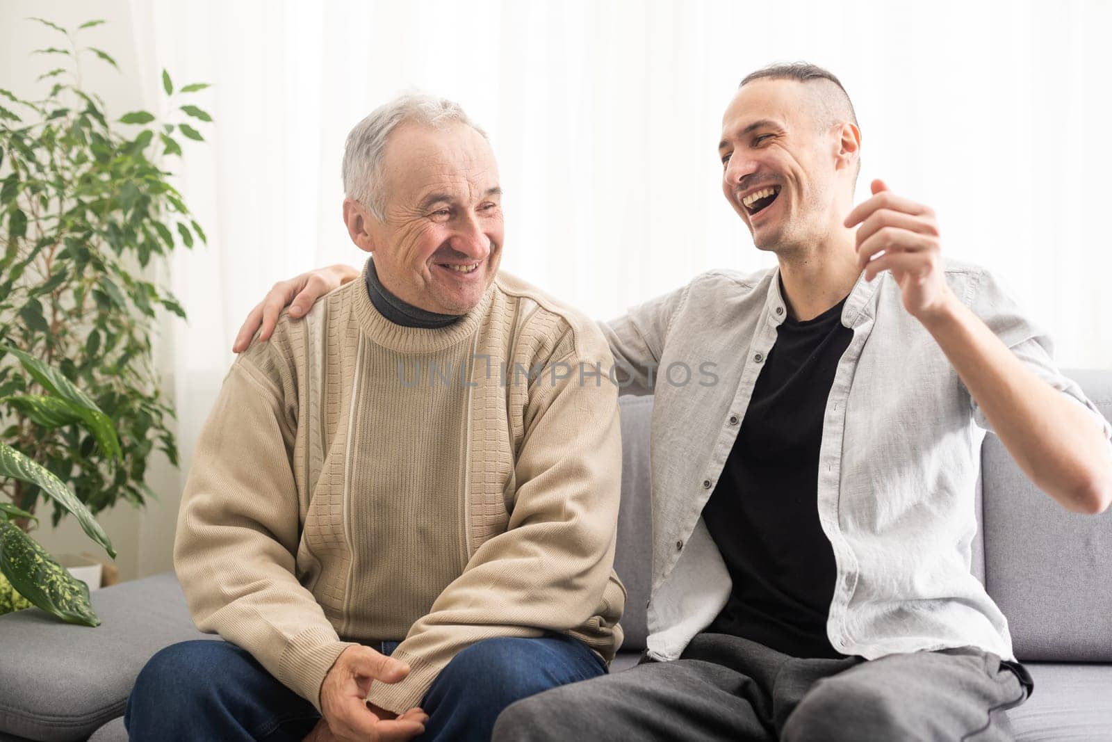 Young adult caucasian son listening and supporting his old elderly senior father at home indoors. Care and love concept