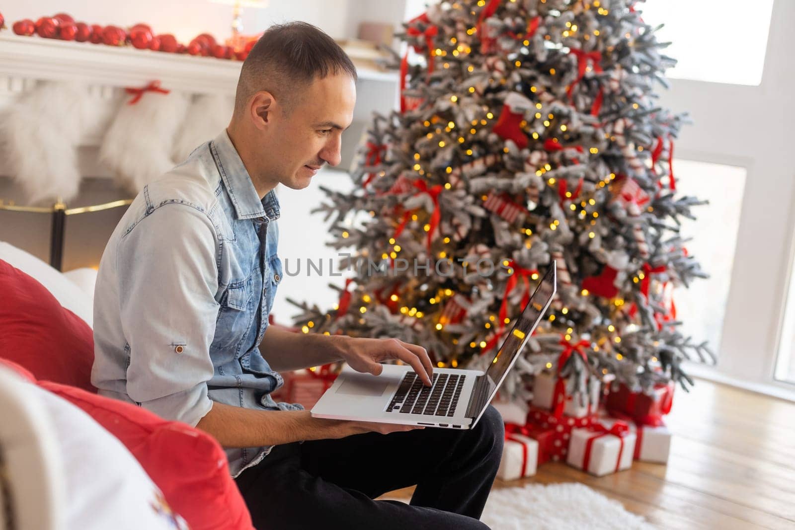 handsome man using laptop computer, talking on video chat call, shopping online. Christmas lights in the background.