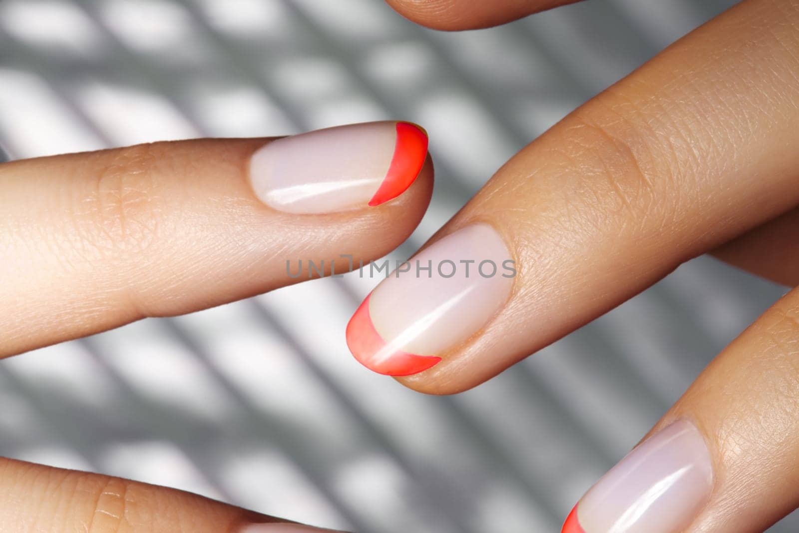 Hands with Trendy Bright Red French Manicure on Geometric Background. Nails Art Design. Close-up of Female Hands with Fashion Neon Nails on Silver Striped Print Background