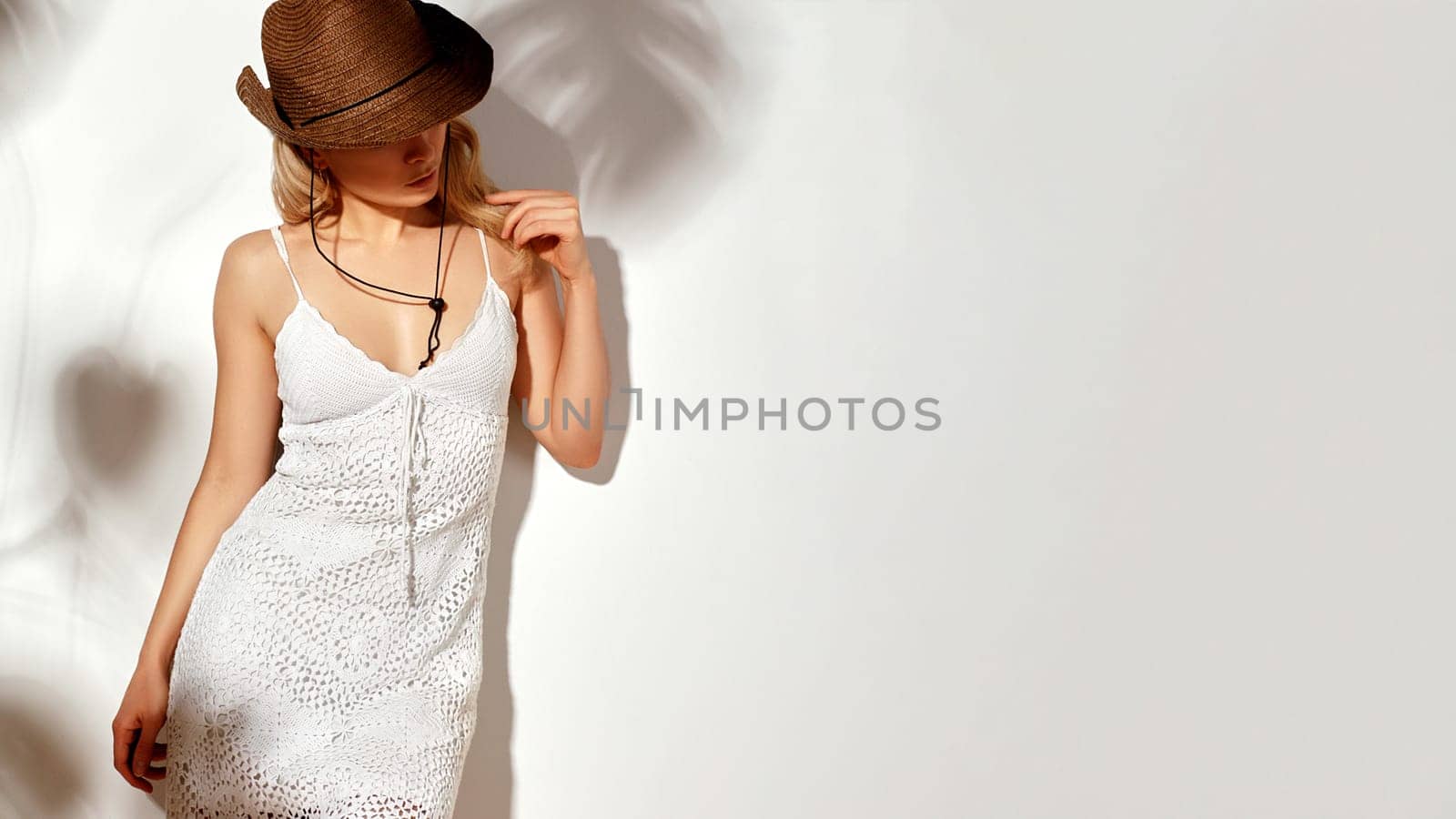 Beautiful Blonde Young Woman Wearing White Crochet Dress and Bown Cowboy Hat under the Shade of Foliage. Bohemic Country Style. Free People in Boho Outfit