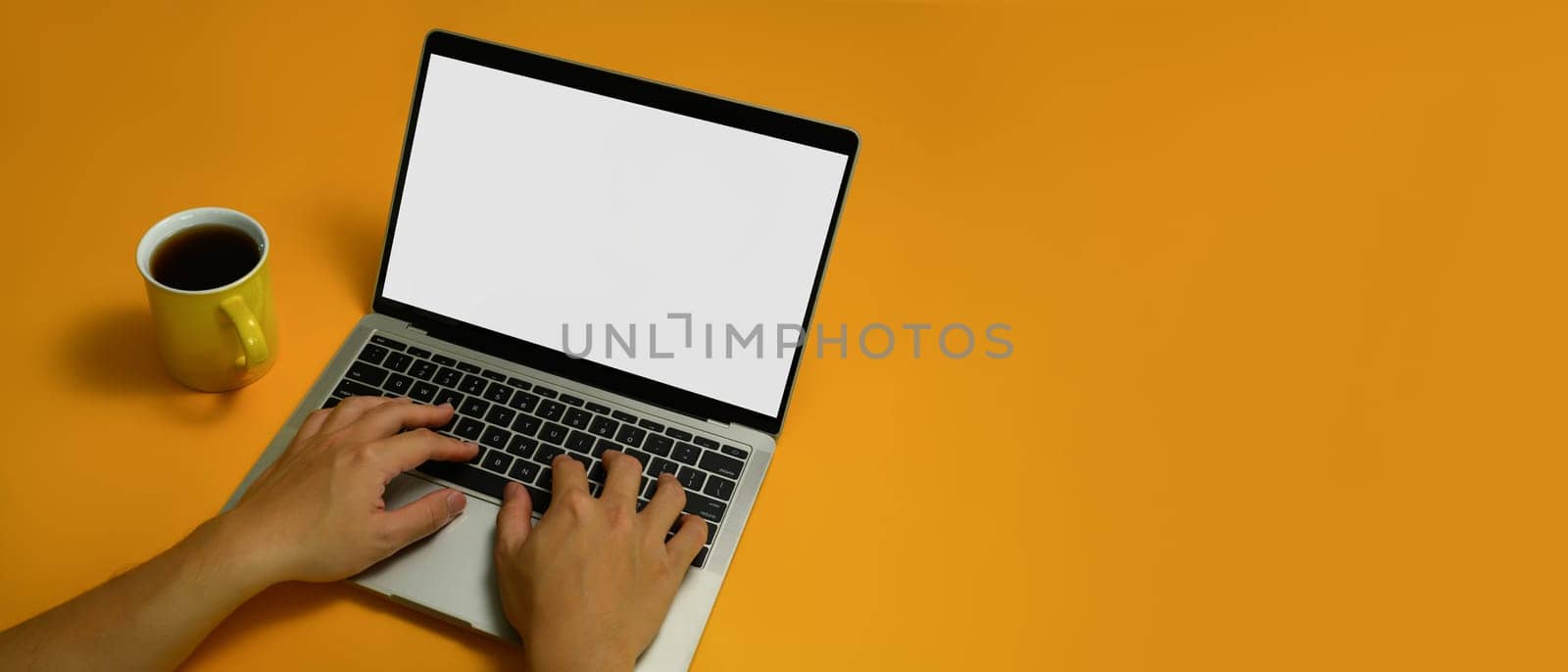 Shot from above view of unrecognizable hands typing on keyboard of laptop computer over yellow background.