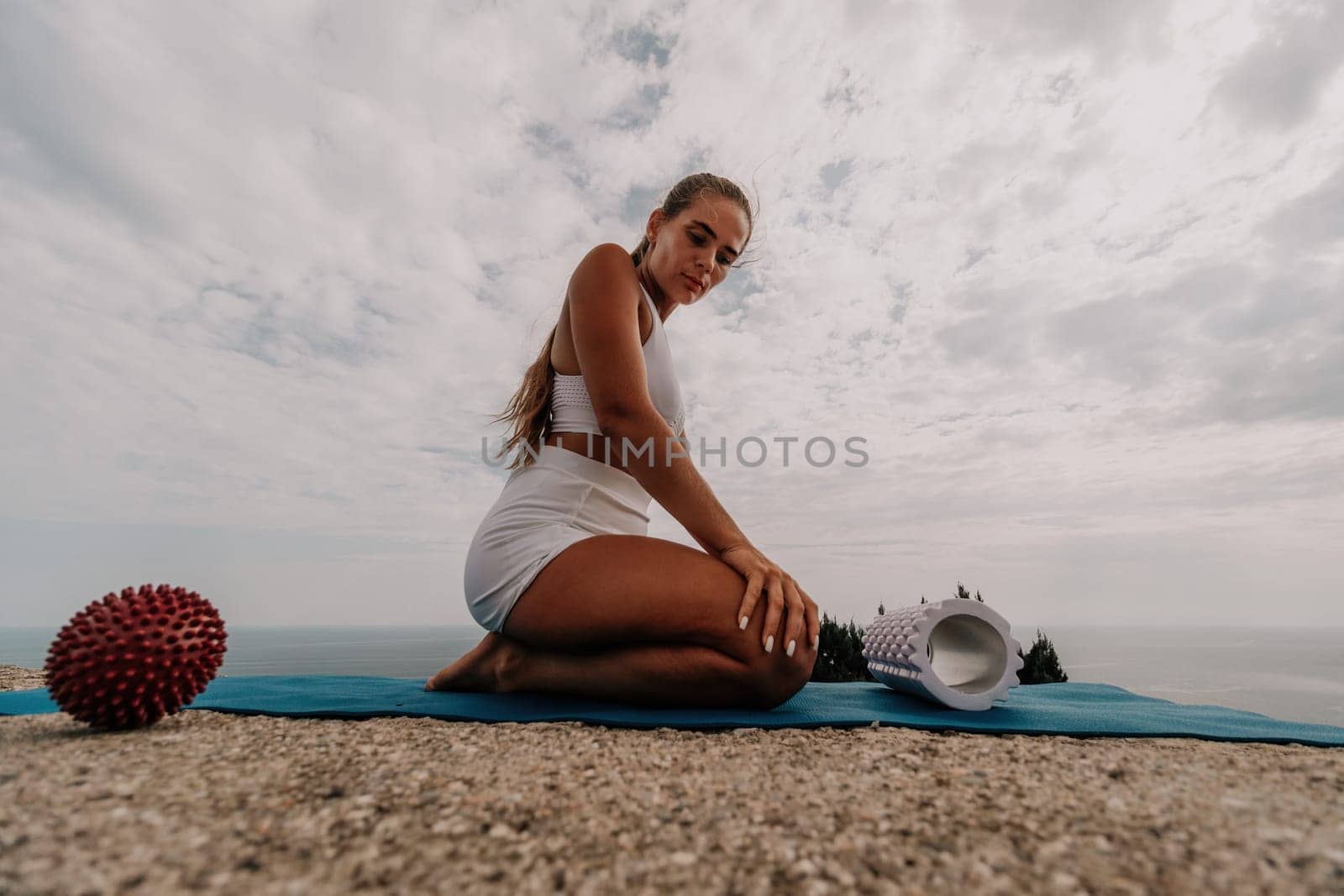 Middle aged well looking woman with black hair doing Pilates with the ring on the yoga mat near the sea on the pebble beach. Female fitness yoga concept. Healthy lifestyle, harmony and meditation.