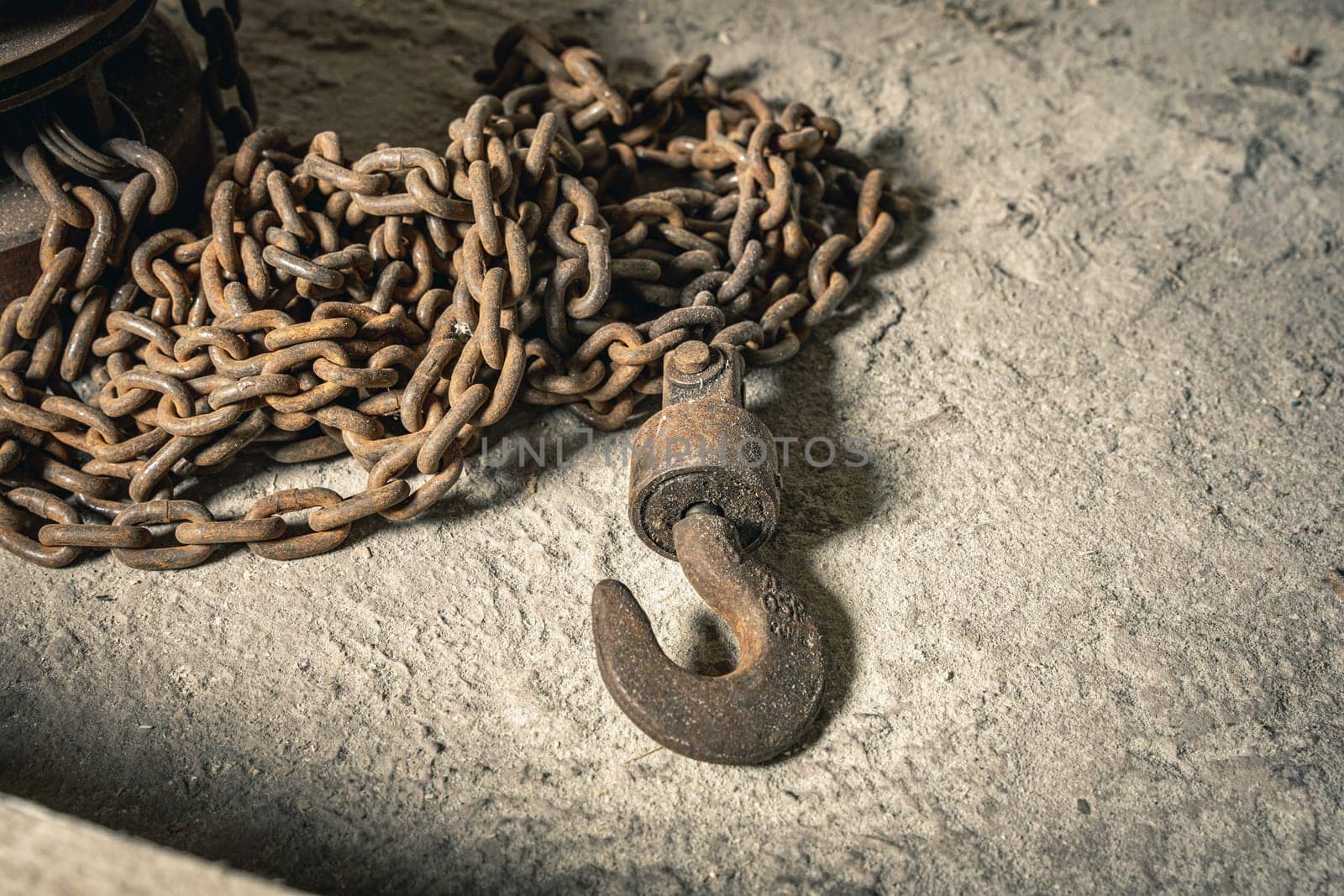 an old rusty iron chain hoist with a thick chain. a large hook for lifting loads. industrial sphere or construction. a functional hoist, dilapidated from time to time. it is used at facilities where reliable and durable lifting mechanisms are required
